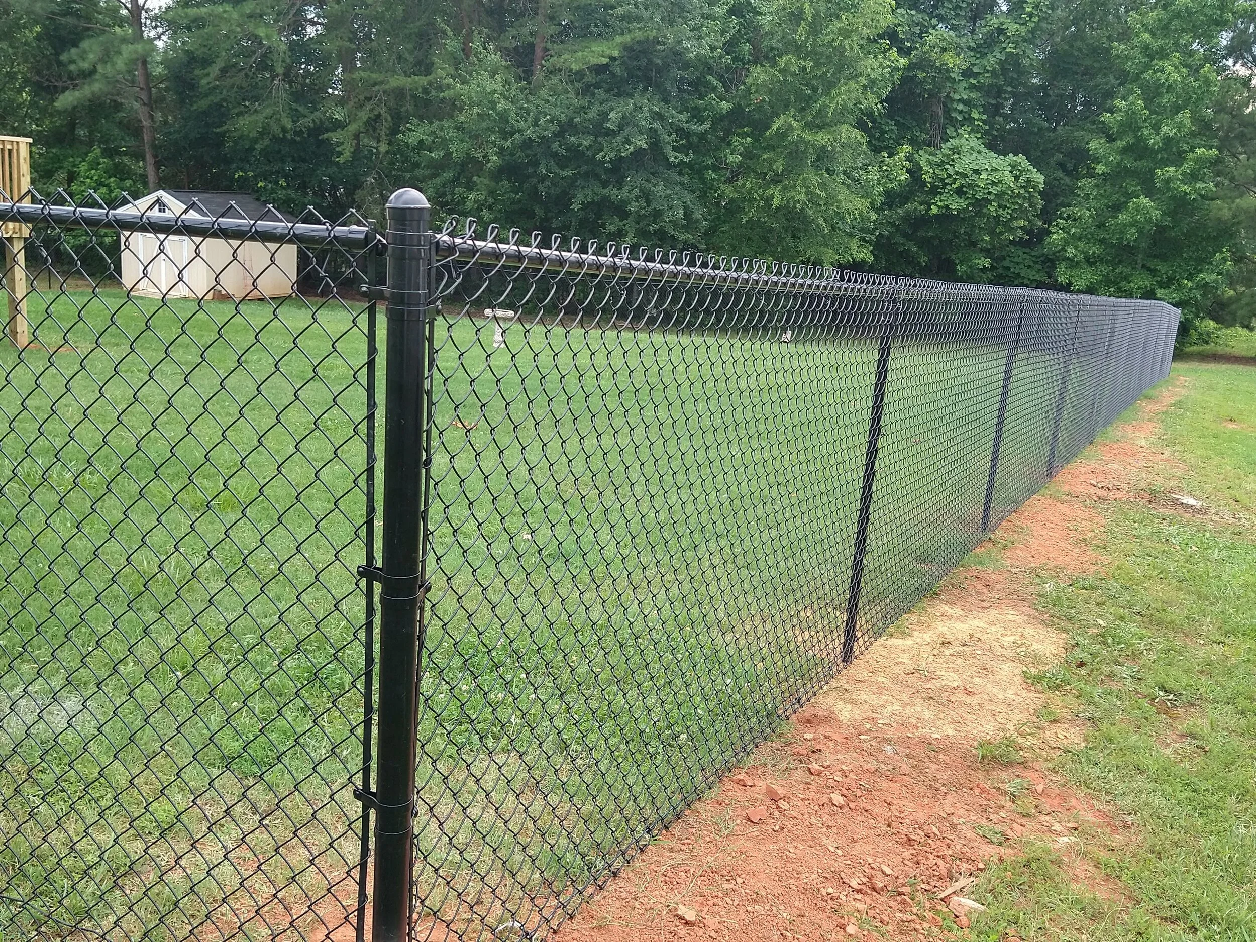 Long black chain-link fence running along a grassy area with trees in the background.