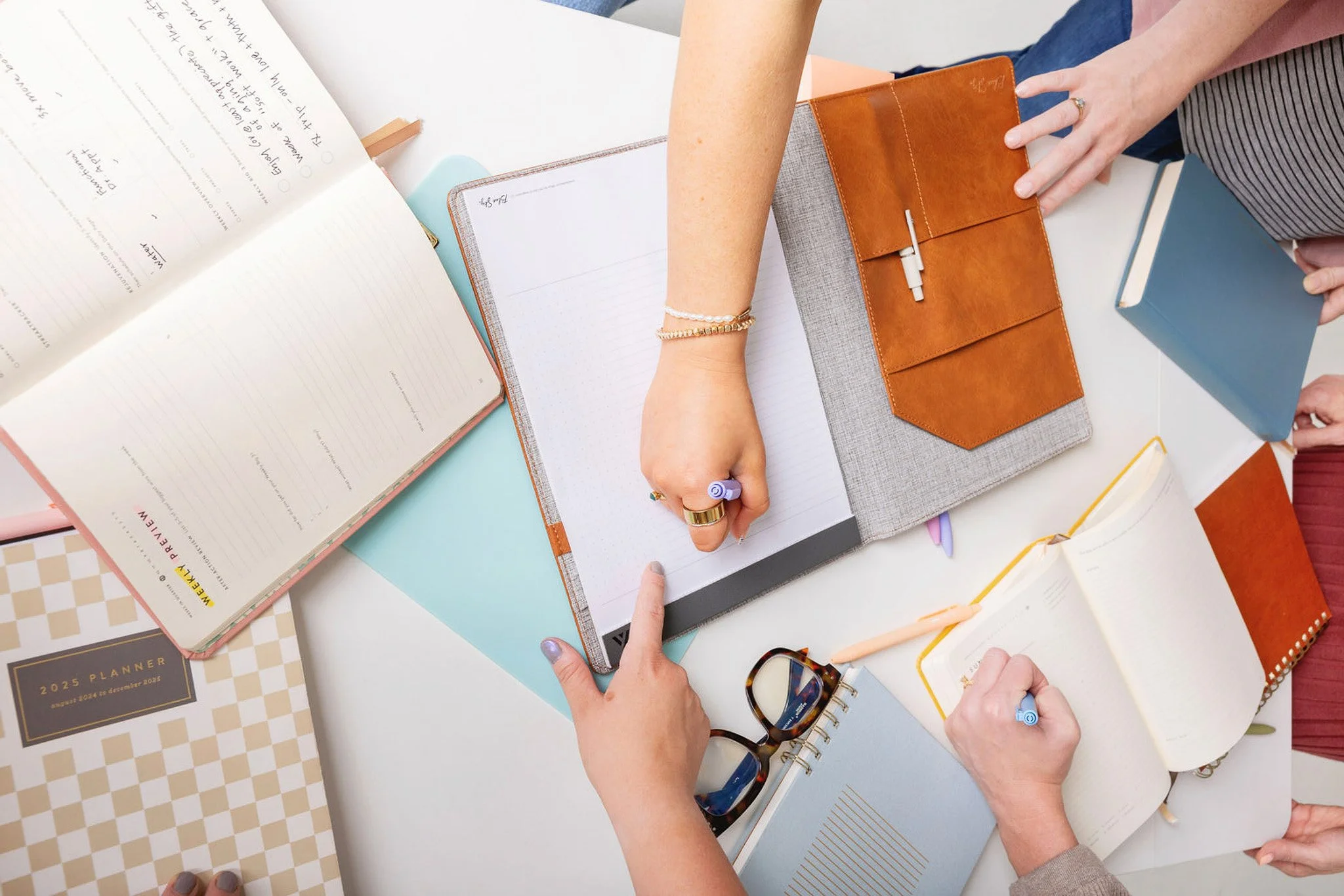 Timely EA's gather around a long, white table filled with colorful books, notebooks, pens, and eyeglasses.