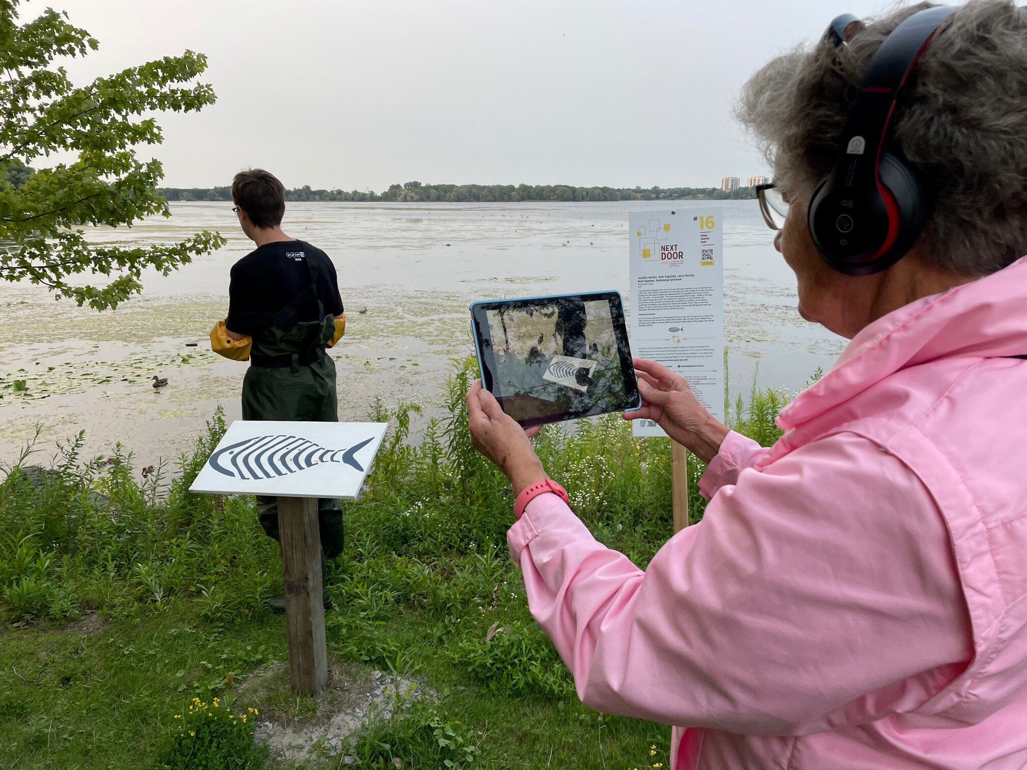 A person holds an iPad over the Sign of the Fish, to view the augmented reality art piece Swimming .