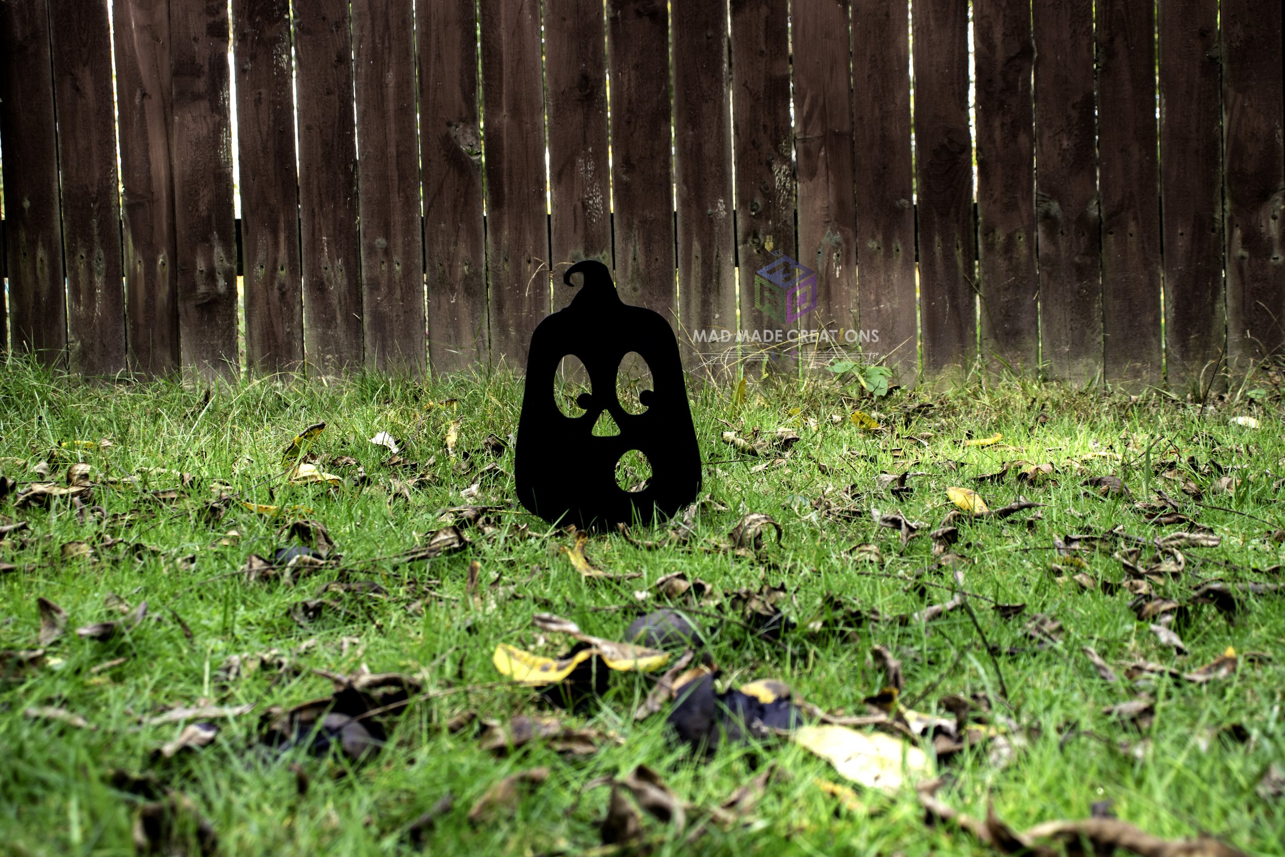 Black 3D printed OH pumpkin Halloween yard stake by MAD Made Creations displayed in grassy backyard during daylight in front of rustic wooden fence