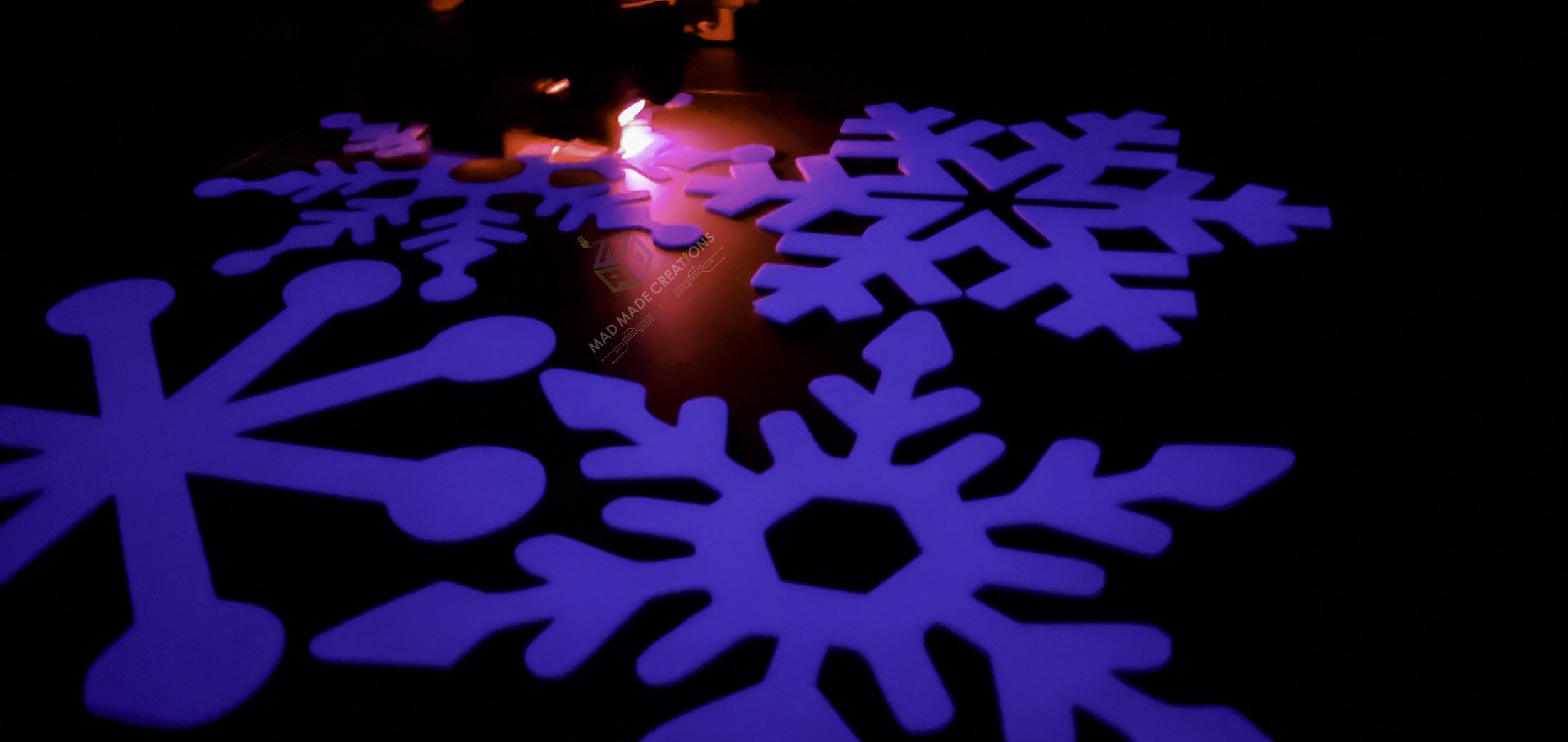 Four 12-inch 3D printed glow-in-the-dark blue snowflakes illuminated mid-print on a large format printer by MAD Made Creations LLC