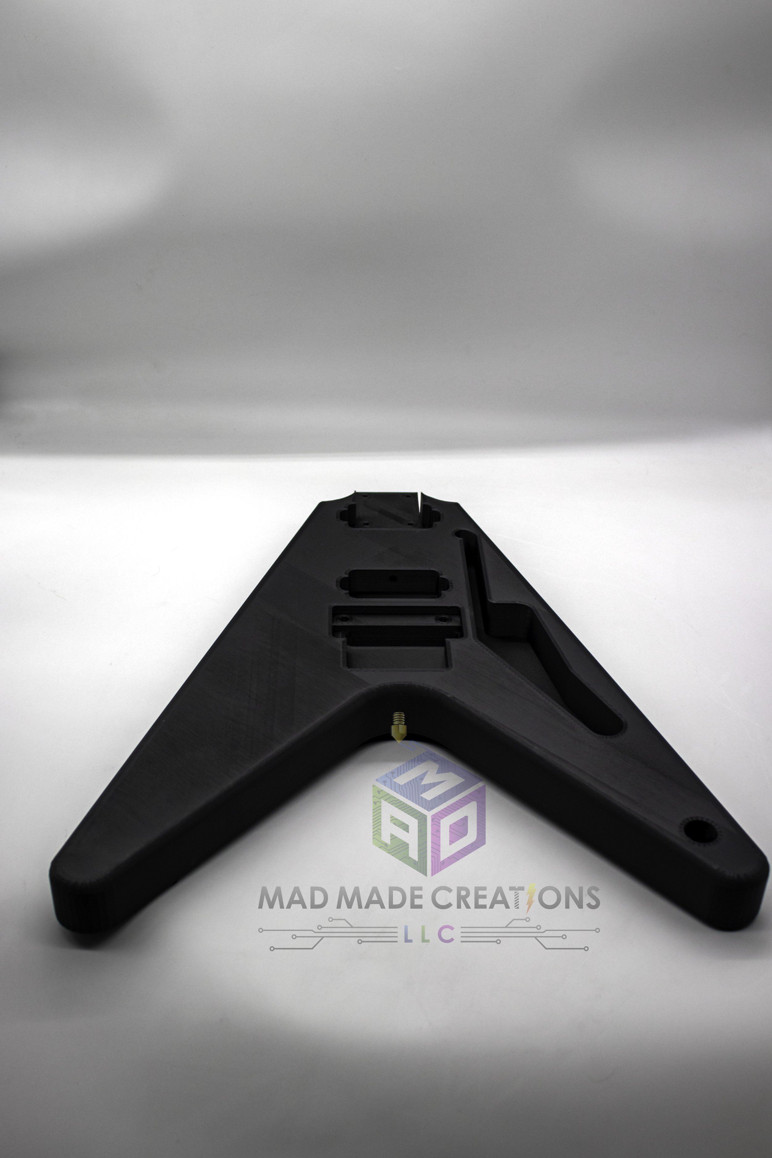 Top front view of custom 1983 Flying V style electric guitar body, 3D printed in black PLA with Floyd Rose tremolo compatibility and HH pickup routing, unpainted and designed by MAD Made Creations LLC