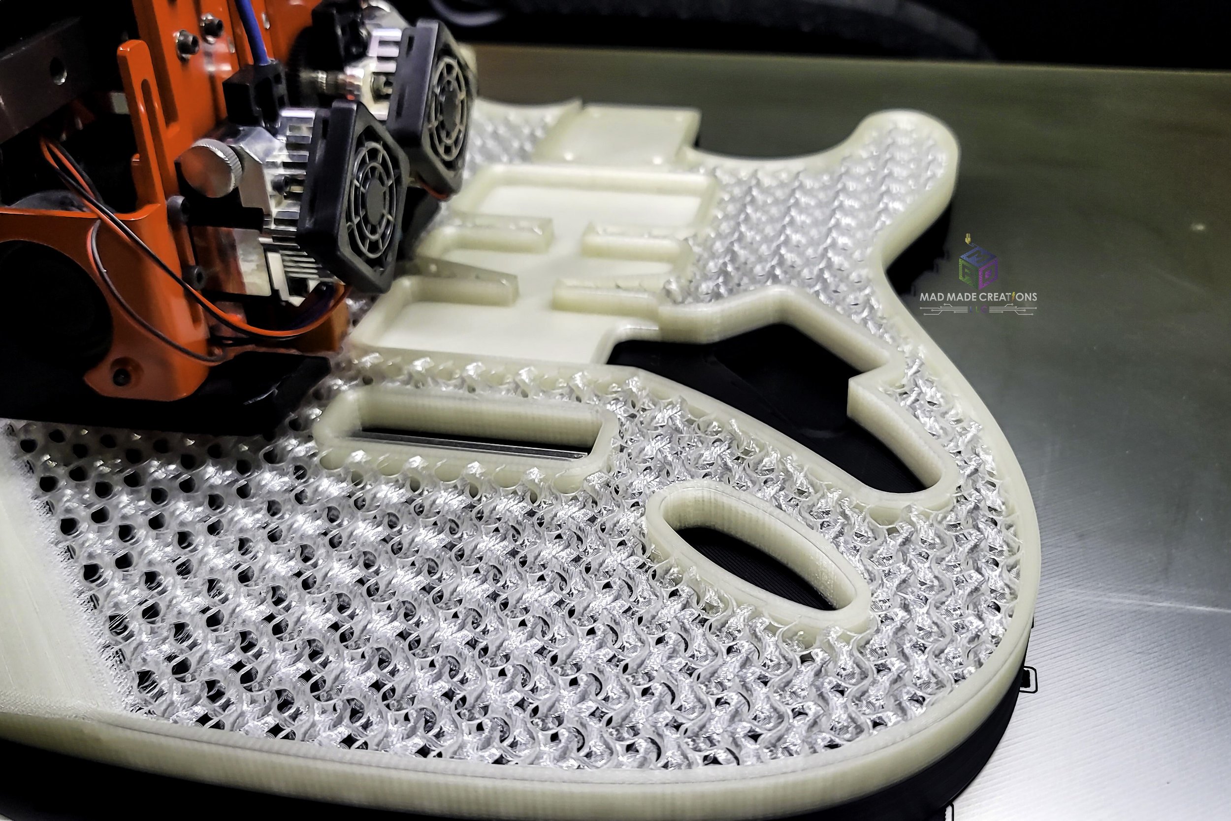 Close-up of HSH Strat-style custom guitar body being 3D printed with glow-in-the-dark filament, featuring Floyd Rose routing and internal gyroid infill by MAD Made Creation