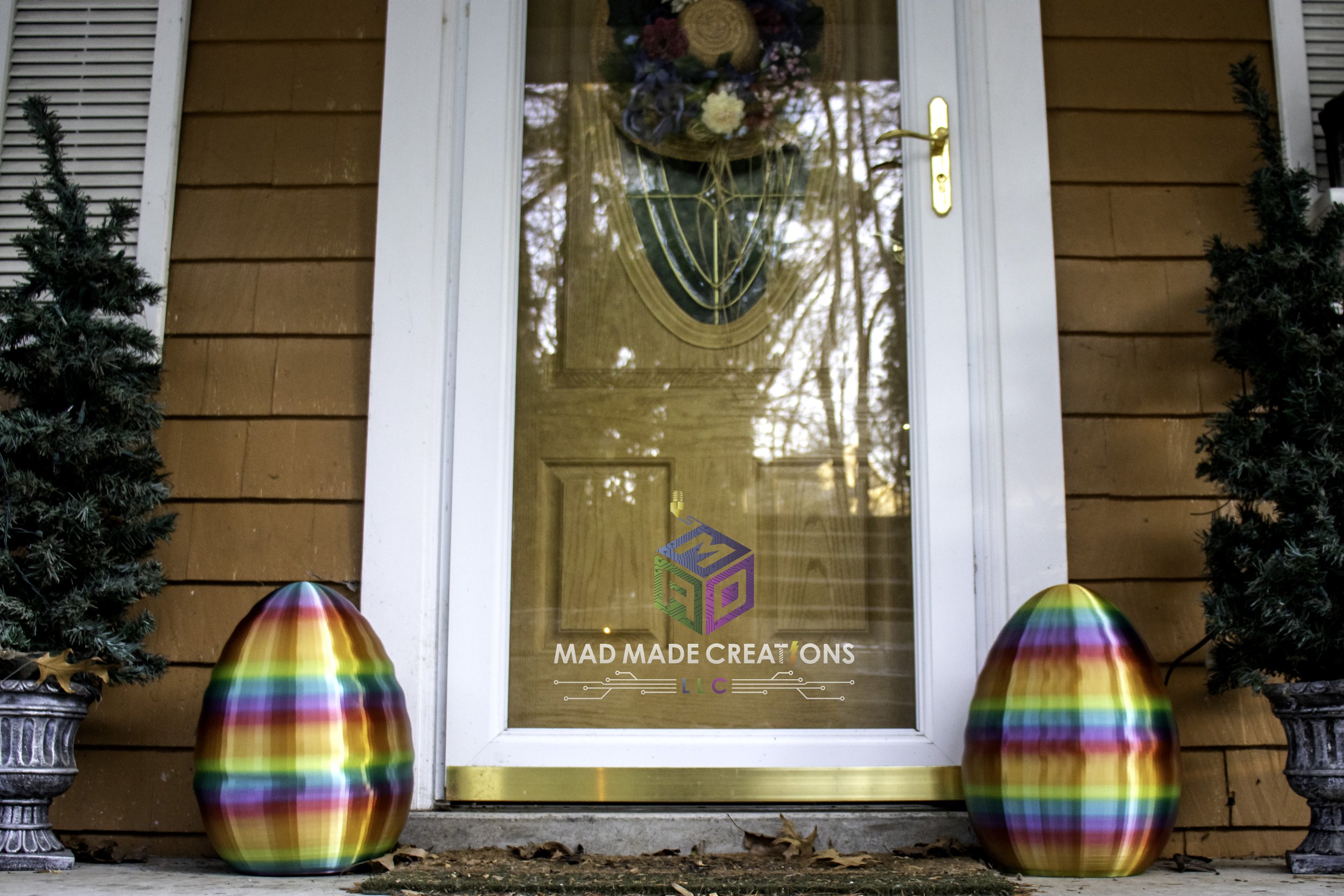 Pair of large rainbow-striped 3D printed Easter eggs displayed on front porch beside door, colorful outdoor spring decoration by MAD Made Creations