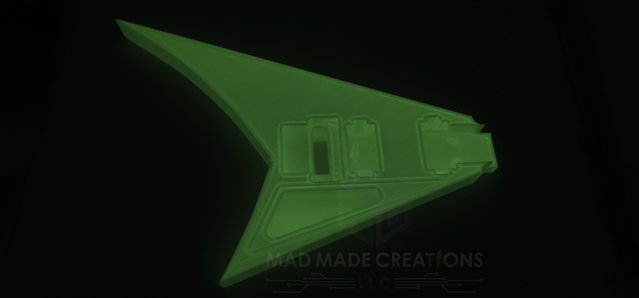 Top-side view of a 3D-printed RR3 Randy Rhoads V-style guitar body glowing green in the dark, routed for HH pickups and Floyd Rose tremolo