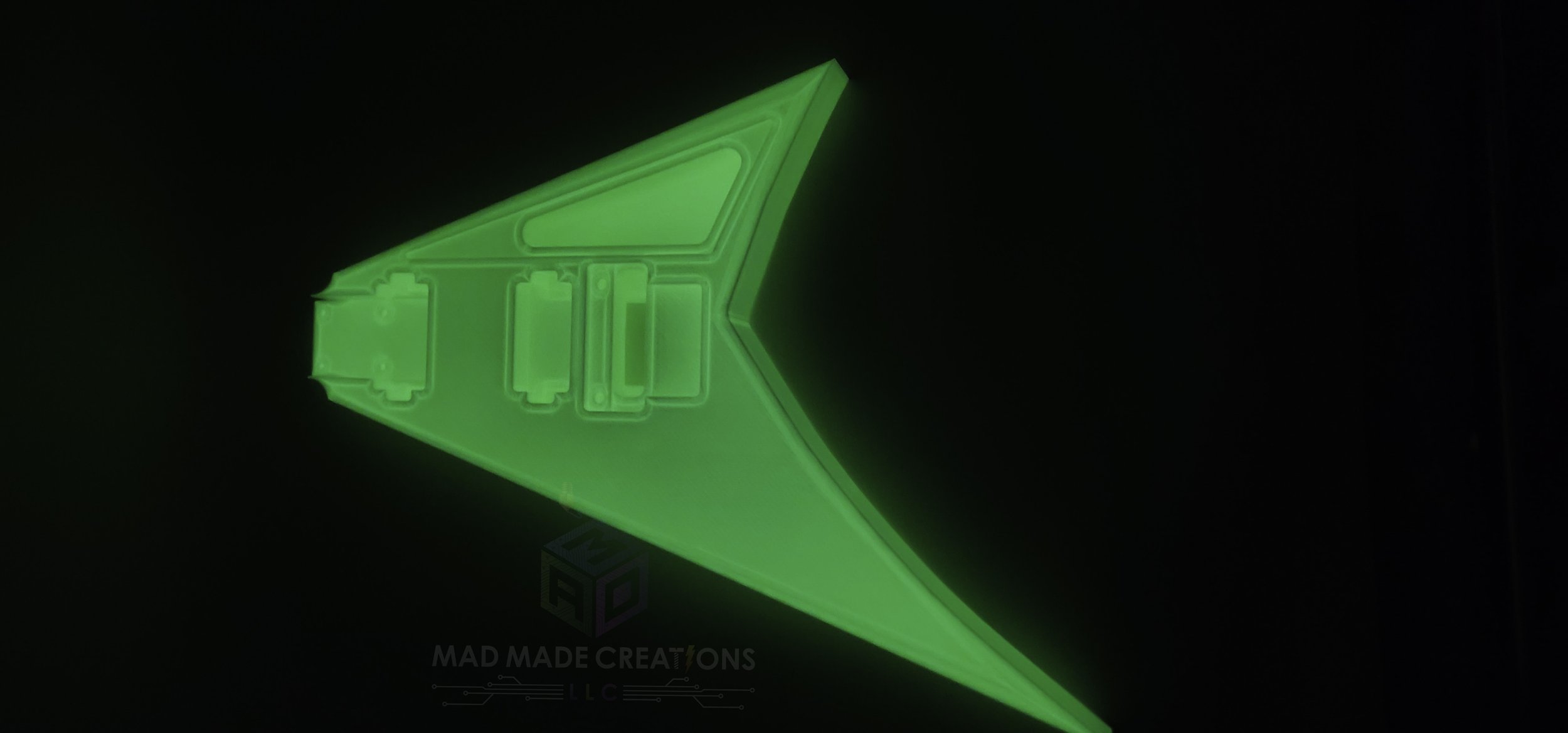 Top angled side view of a glowing green 3D-printed Randy Rhoads V-style guitar body with HH pickup routing and Floyd Rose cavity, showcased in the dark