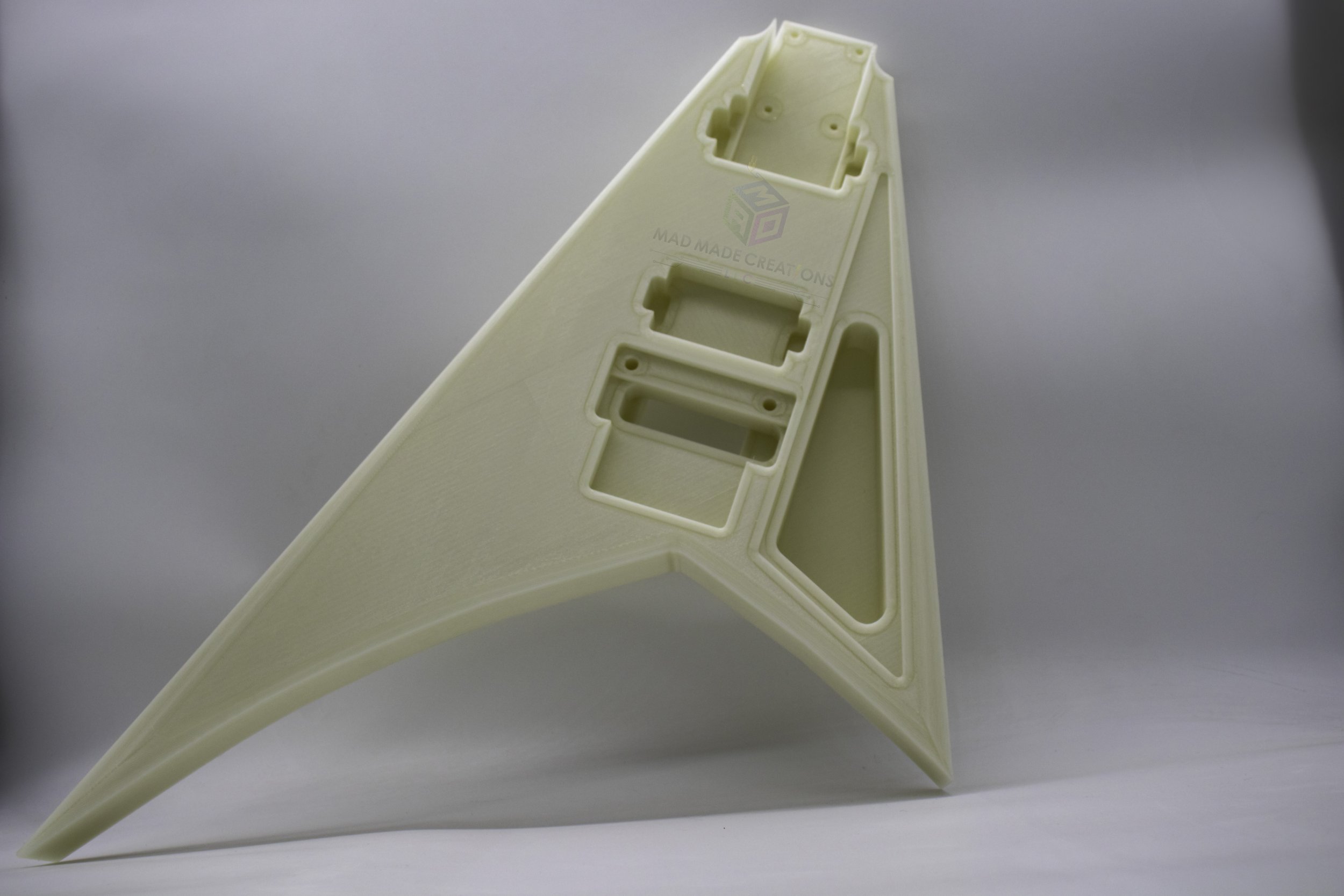 Front view of 3D-printed Randy Rhoads V-style guitar body standing upright, in natural light, showcasing HH pickup routing and Floyd Rose cavity in glow-in-the-dark material