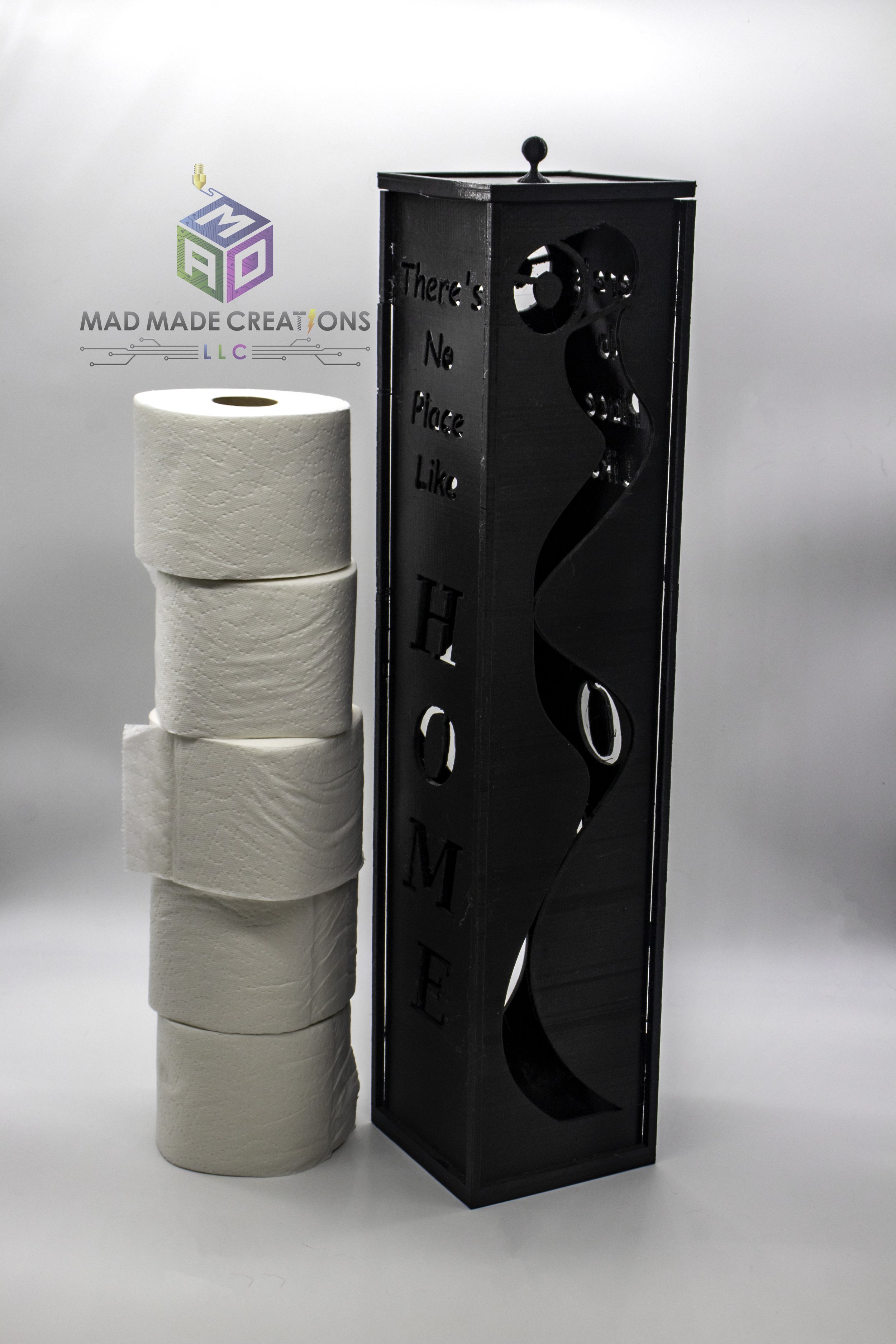 Custom 3D printed vertical toilet paper holder with decorative text 'There's No Place Like Home,' black design with curved cutout, shown beside stacked toilet paper rolls – MAD Made Creations