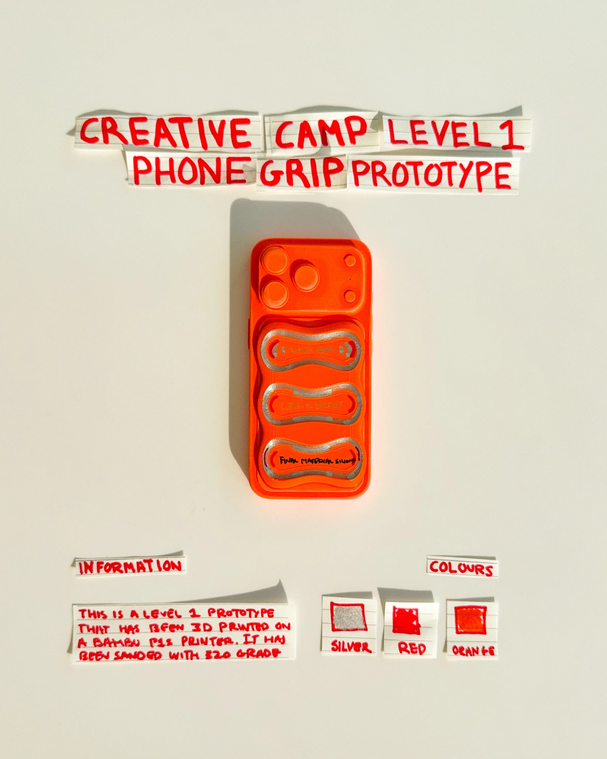 day 28 prototype 26: experiment with an orange rectangular phone grip featuring sculpted horizontal openings and handwritten graphics. the design explores surface texture, raised details and the relationship between function and visual expression.