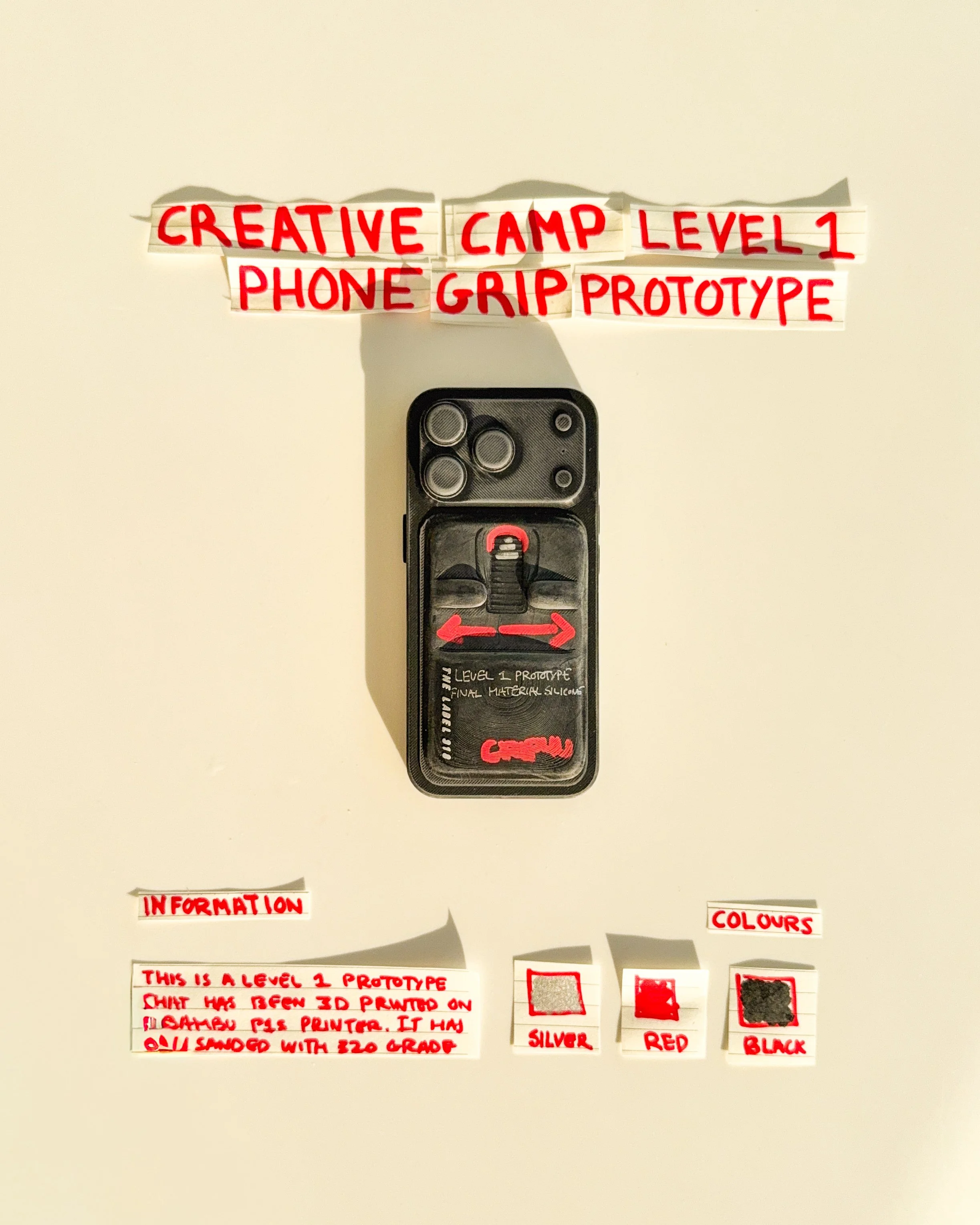 day 13 prototype 11: develop a rectangular phone grip with a horizontal finger opening, red accents and handwritten typography. the design explores the relationship between finger placement, function and graphic details.