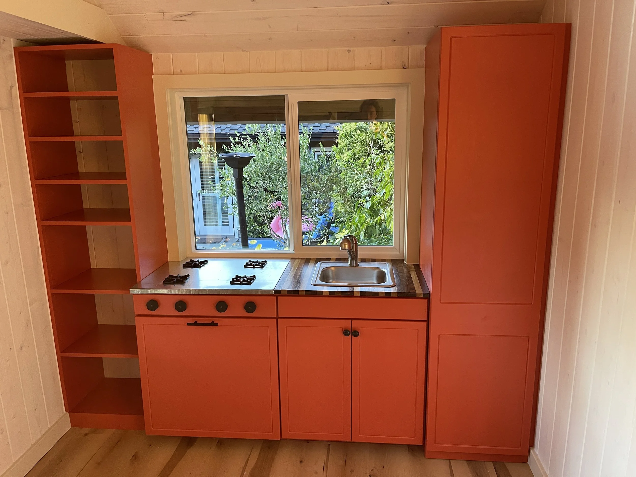 Playhouse kitchen done in a bold orange and surrounded with whitewashed walls.