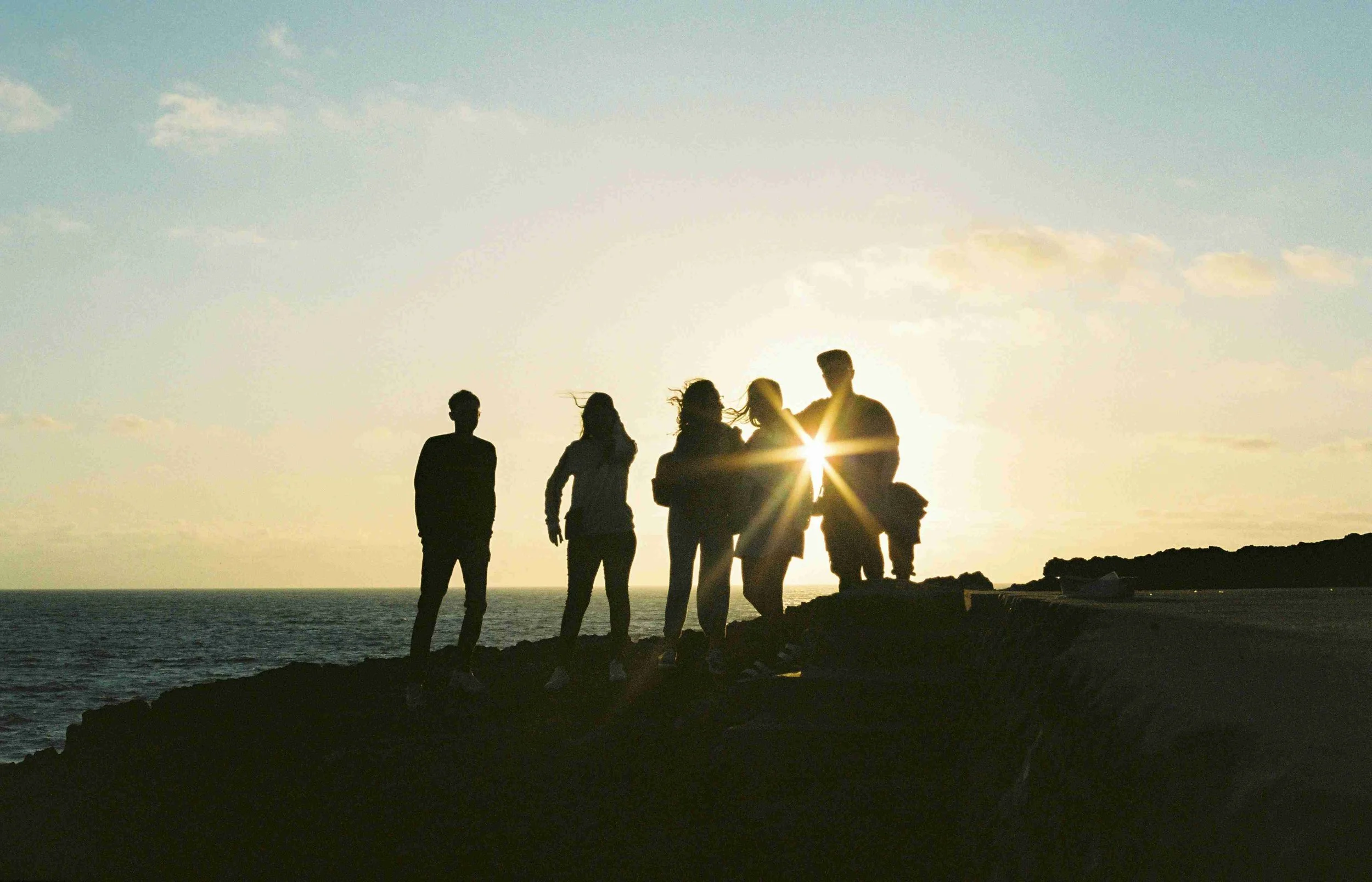 This image is clickable. Group of students are standing on the beach during the sunset