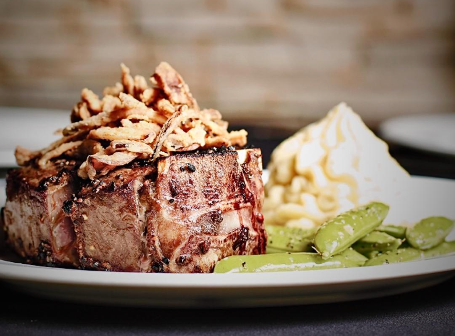 A plate with a cooked meat portion topped with mushrooms, with mashed potatoes and green beans on the side.