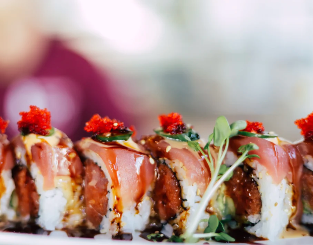 Close-up of a sushi roll topped with red tobiko, sliced crab, cucumber, and drizzled with eel sauce, garnished with microgreens.