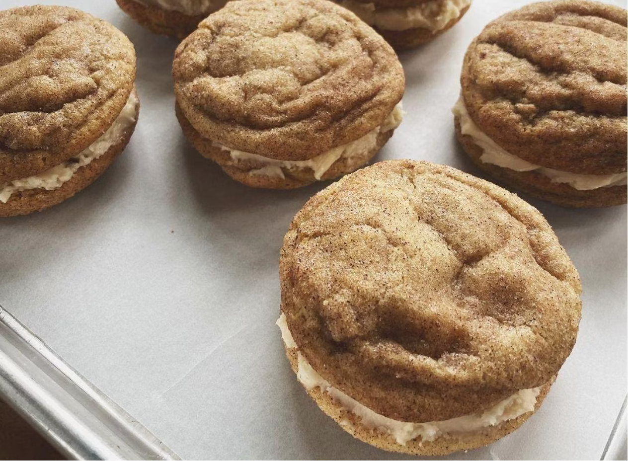 Close-up of several sandwich cookies with a crumbly, brown sugar-spiced top and cream filling, placed on parchment paper.