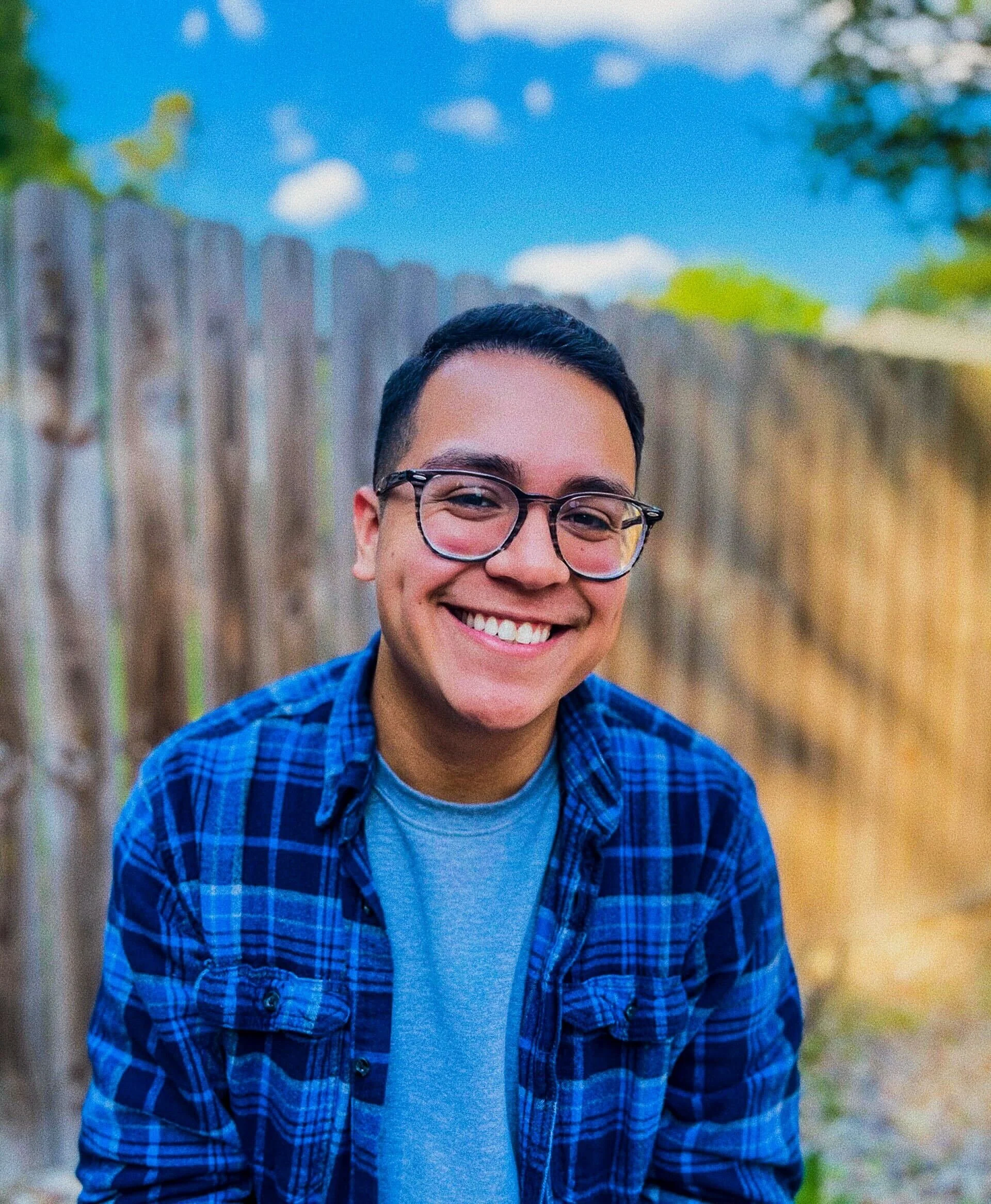 A headshot of Alejandro, wearing a black and blue flannel and smiling.