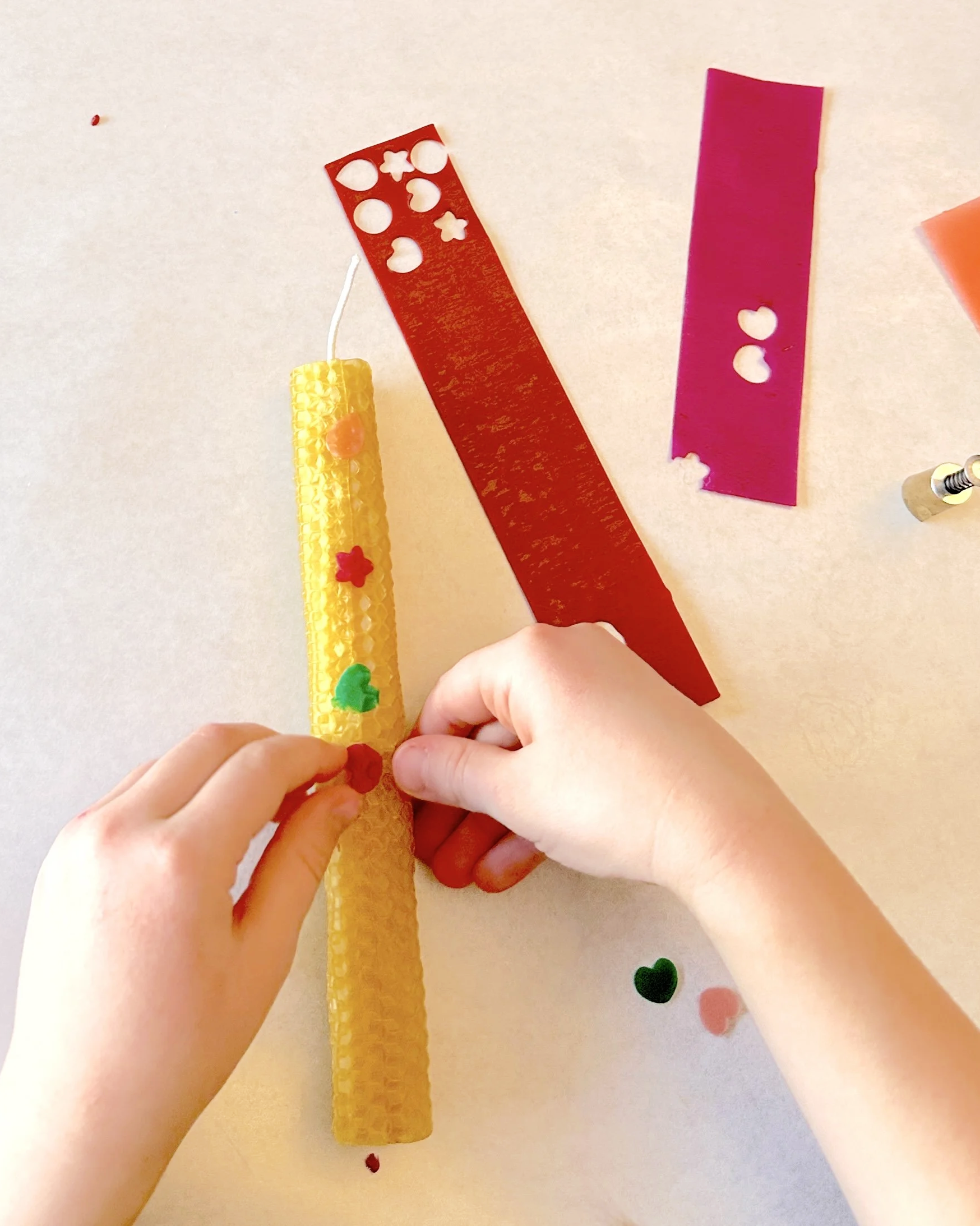 young child adding punched wax designs to handmade beeswax candle