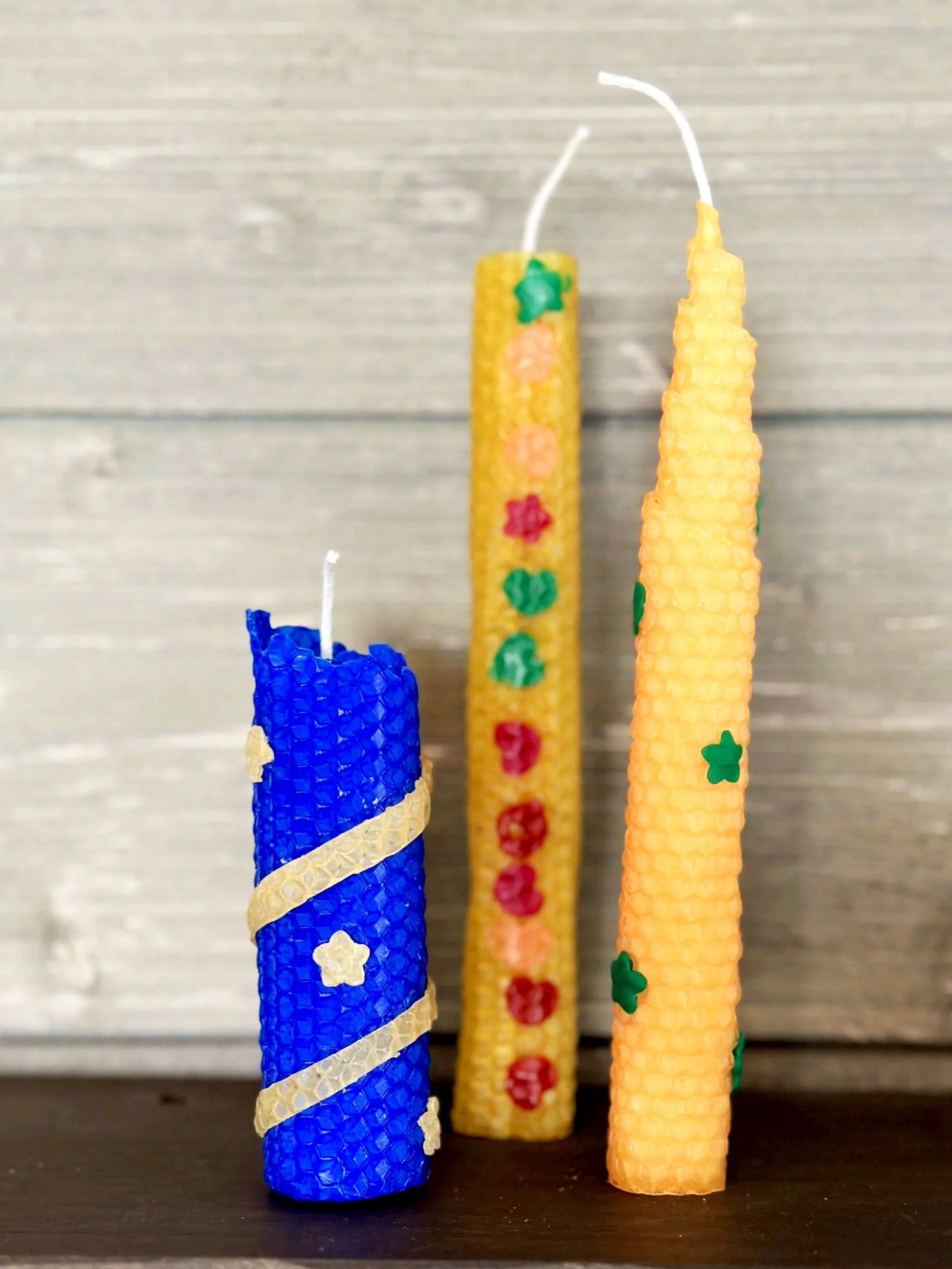 3 handmade rolled beeswax candles in natural and blue colors positioned in front of a grey background