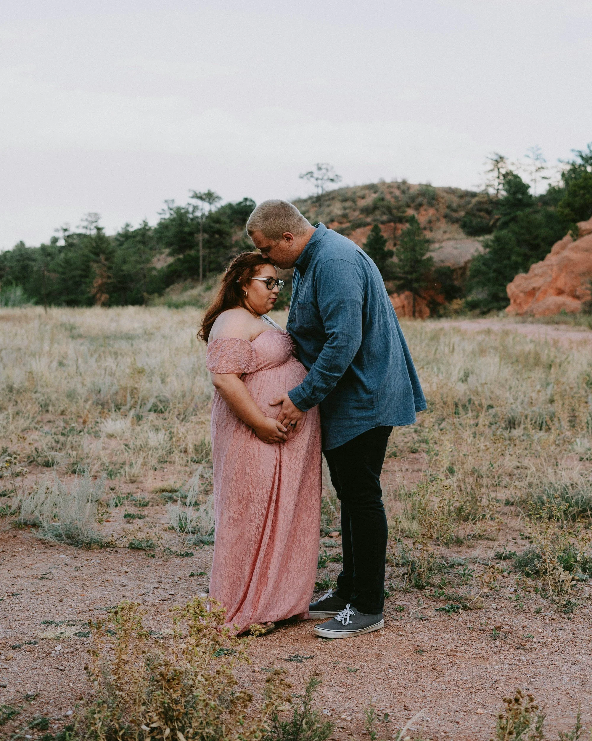 A pregnant couple hugging in a field.