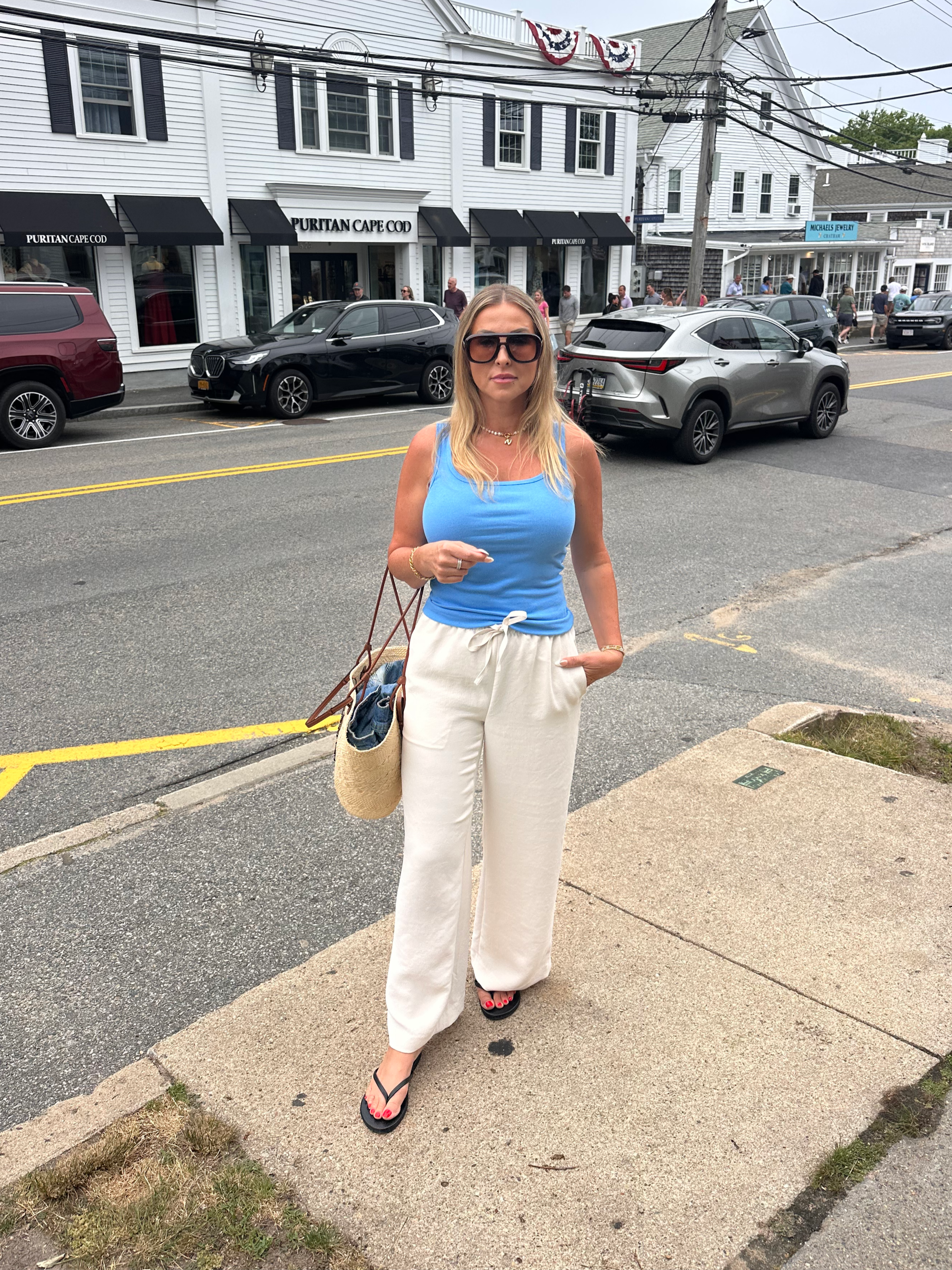 Comfortable summer capsule wardrobe outfit with a blue tank, white linen-style pants, woven tote, and simple accessories for a Cape Cod vacation.