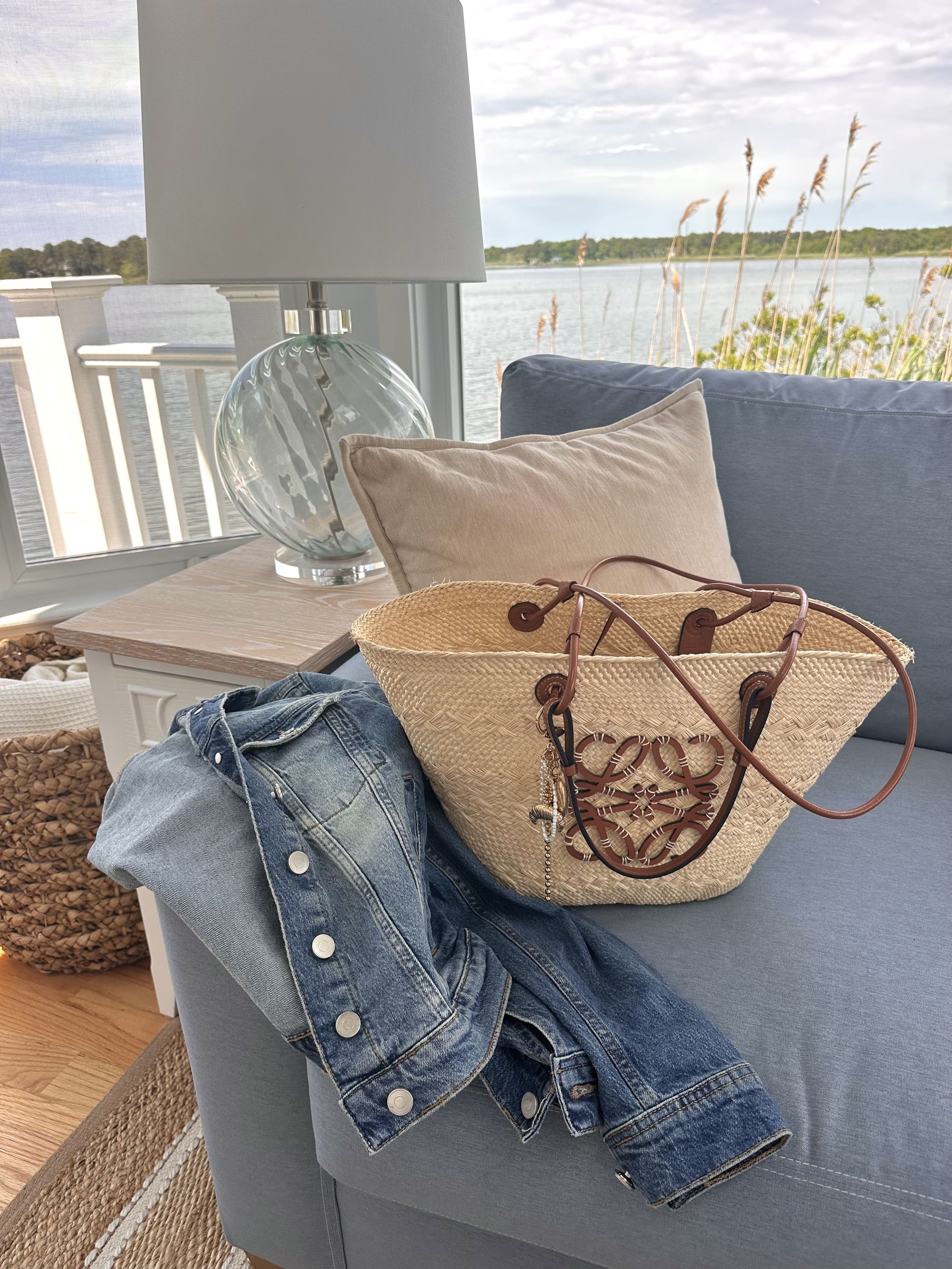 Classic summer travel accessories including a denim jacket and woven tote bag overlooking the water in Cape Cod.