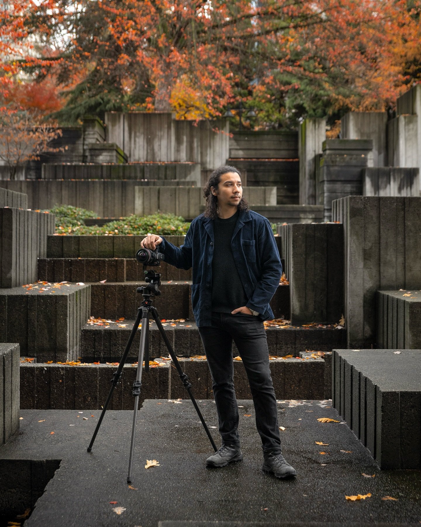 Photographer Santiago Leon standing with a tripod at Freeway Park in Seattle, surrounded by modern concrete architecture and fall trees.