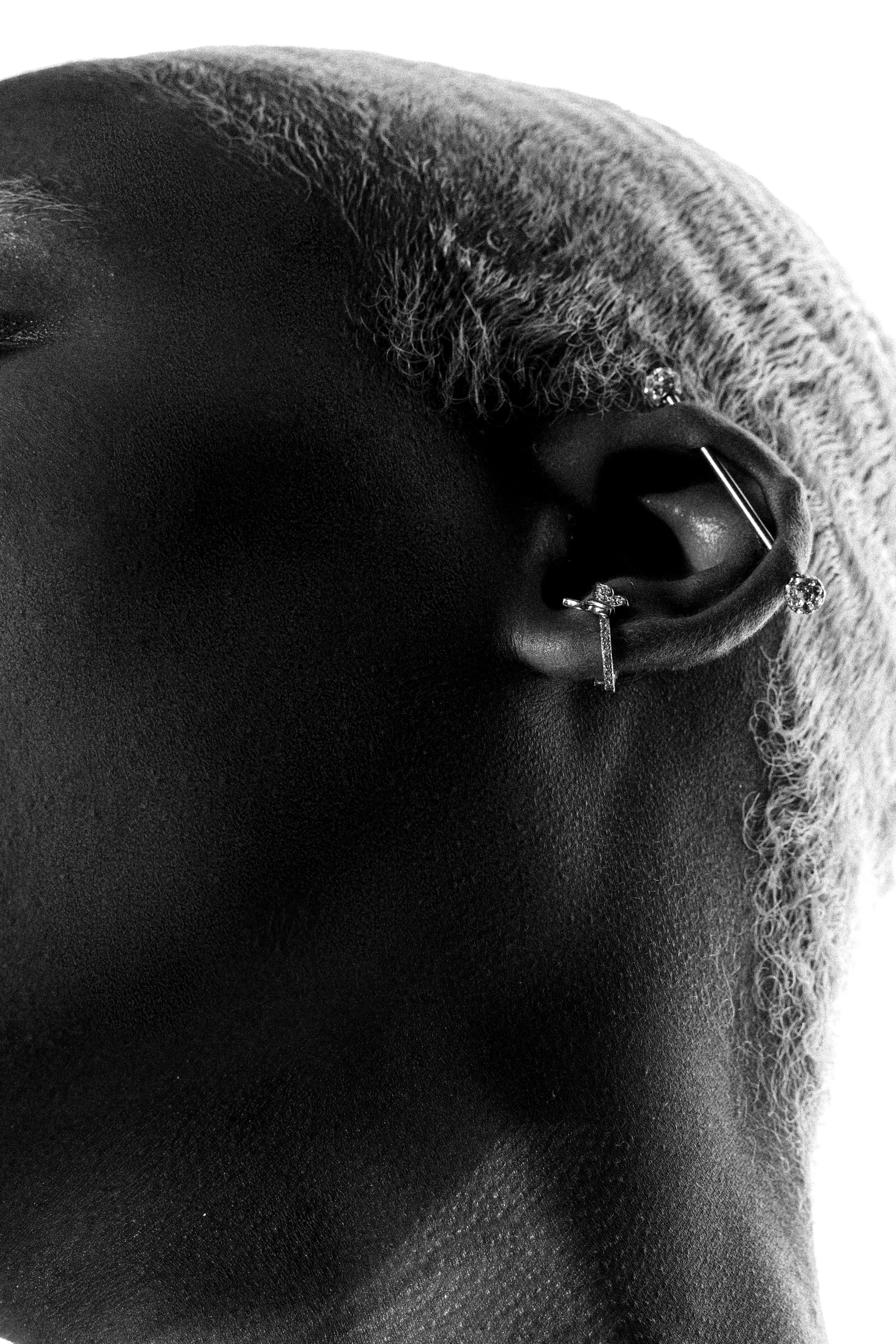 Close-up black and white photo of a person's ear with earrings, textured hair, and smooth skin.