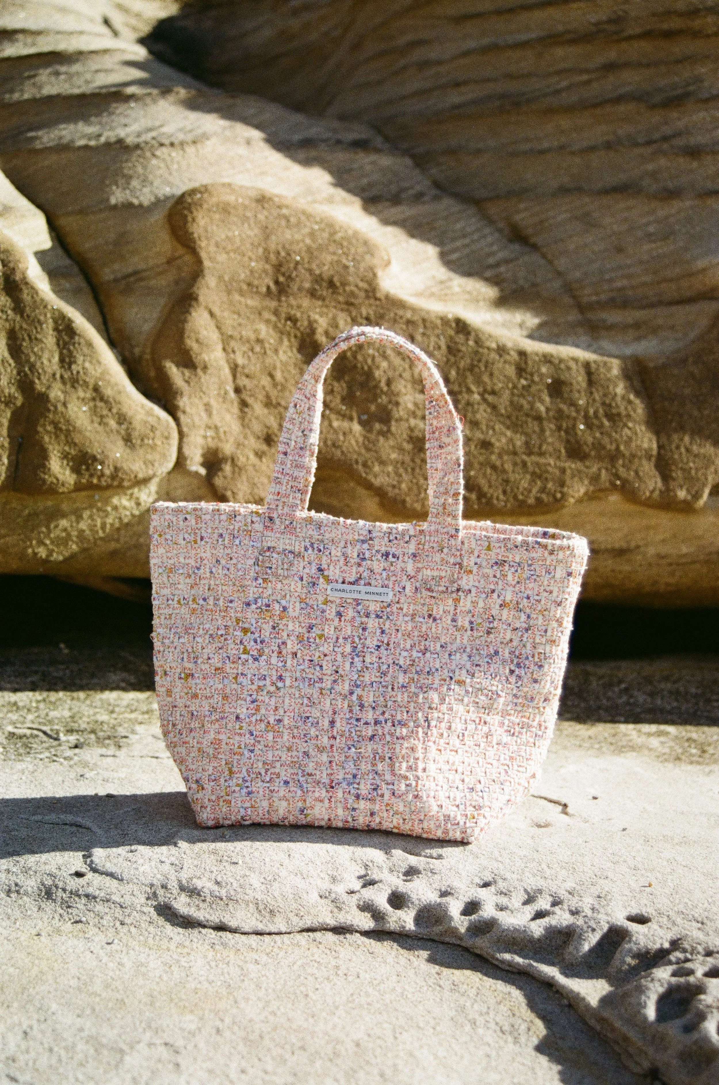 A patterned tote bag resting on sandy terrain with rocks in the background.