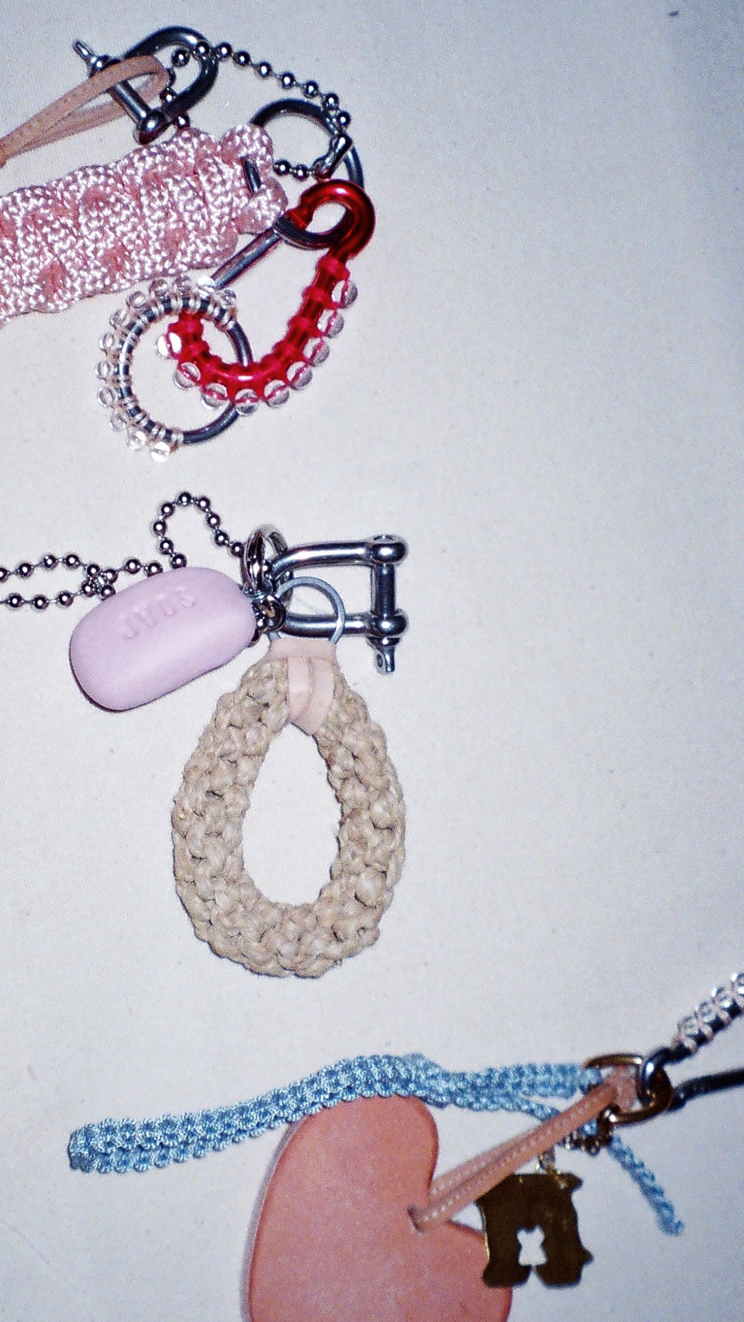 Close-up of various colorful keychains and charms, including a pink heart, a beige woven loop, a pink soap-shaped charm, and other small accessories.