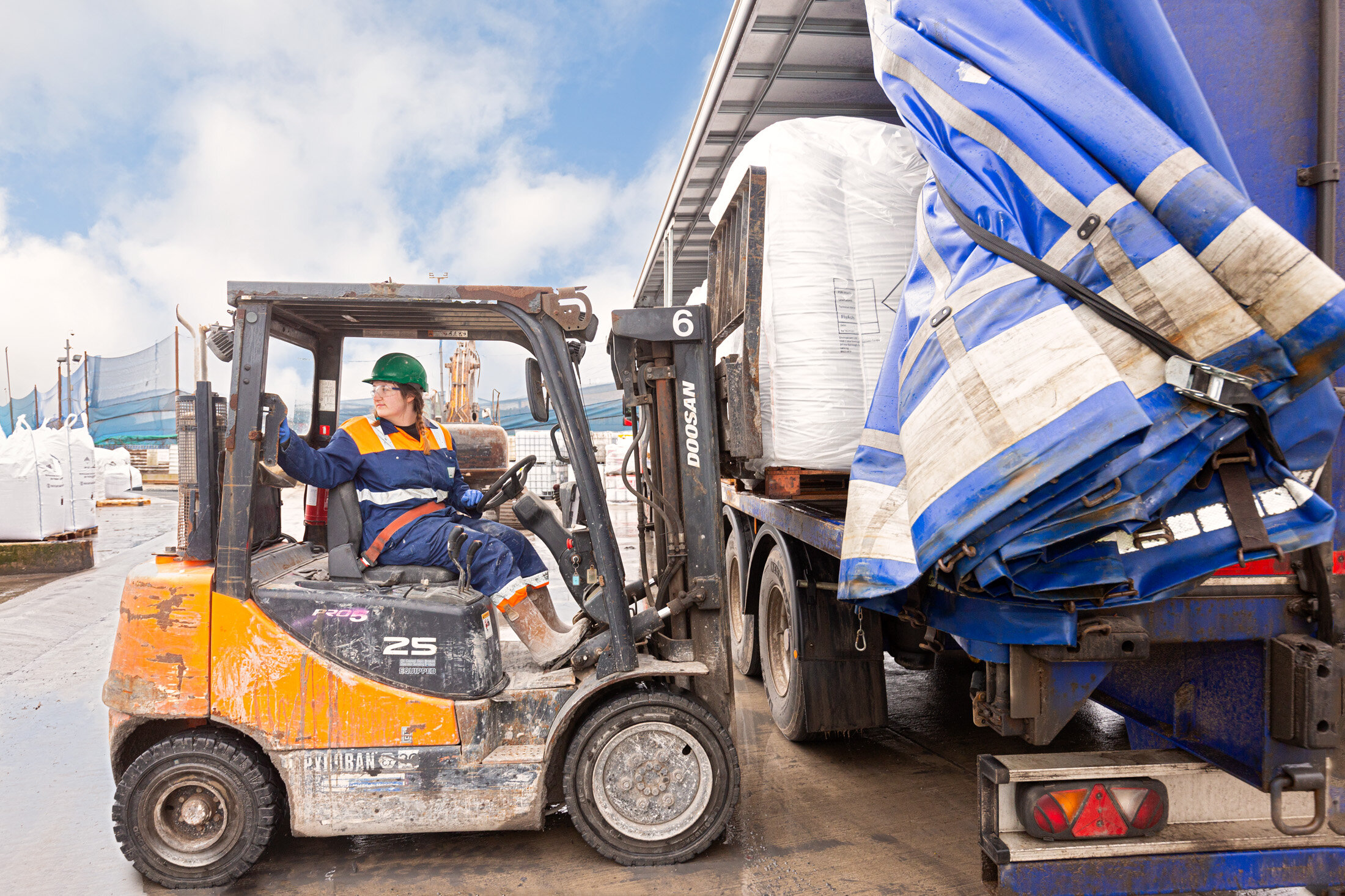 Woman in PPE reversing a Doosan forklift truck, unloading bagged APCr from a lorry trailer for a UK waste management company