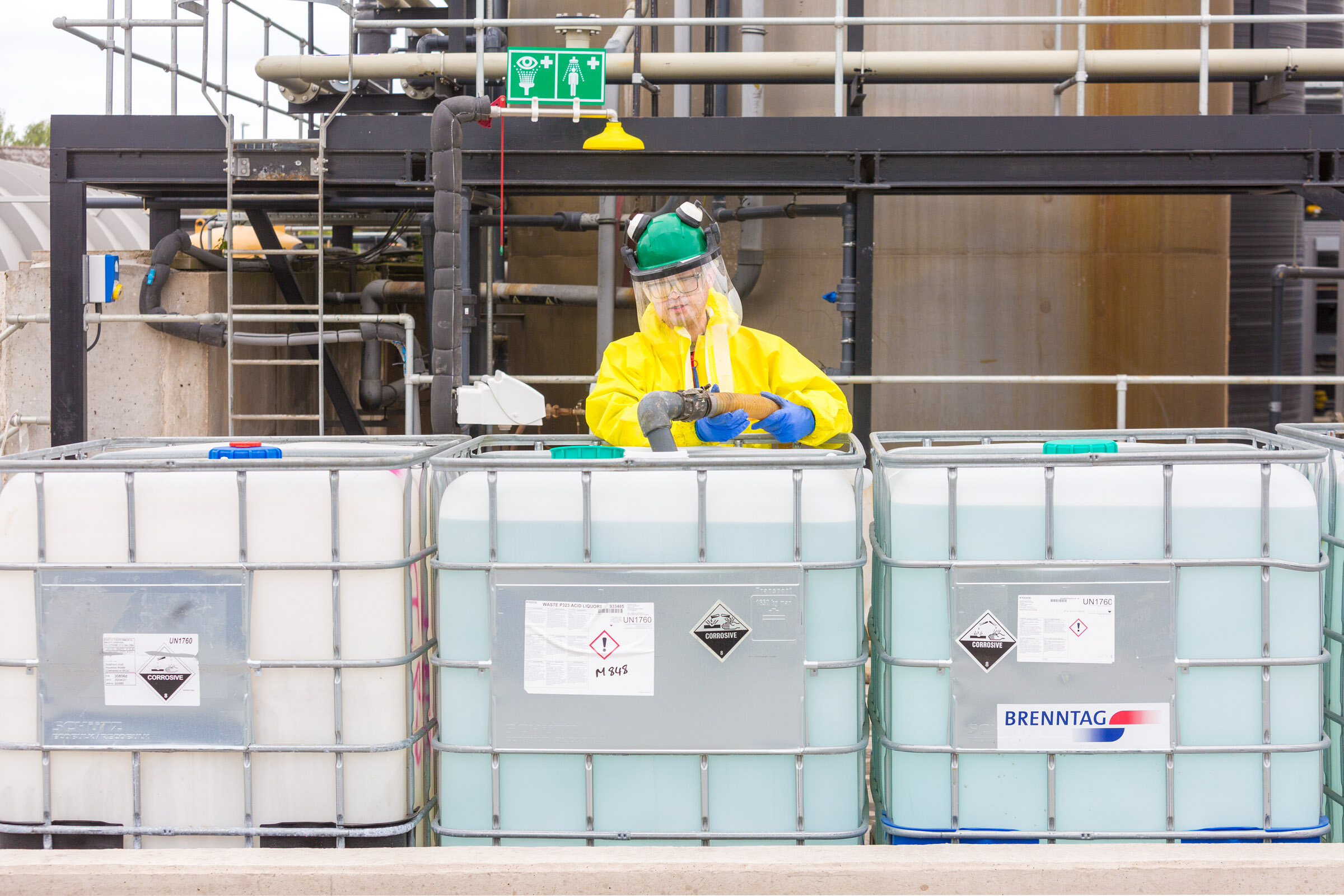 Man in yellow hazmat suit &amp; PPE, pumping waste acid for neutralisation into an IBC for a UK waste management company