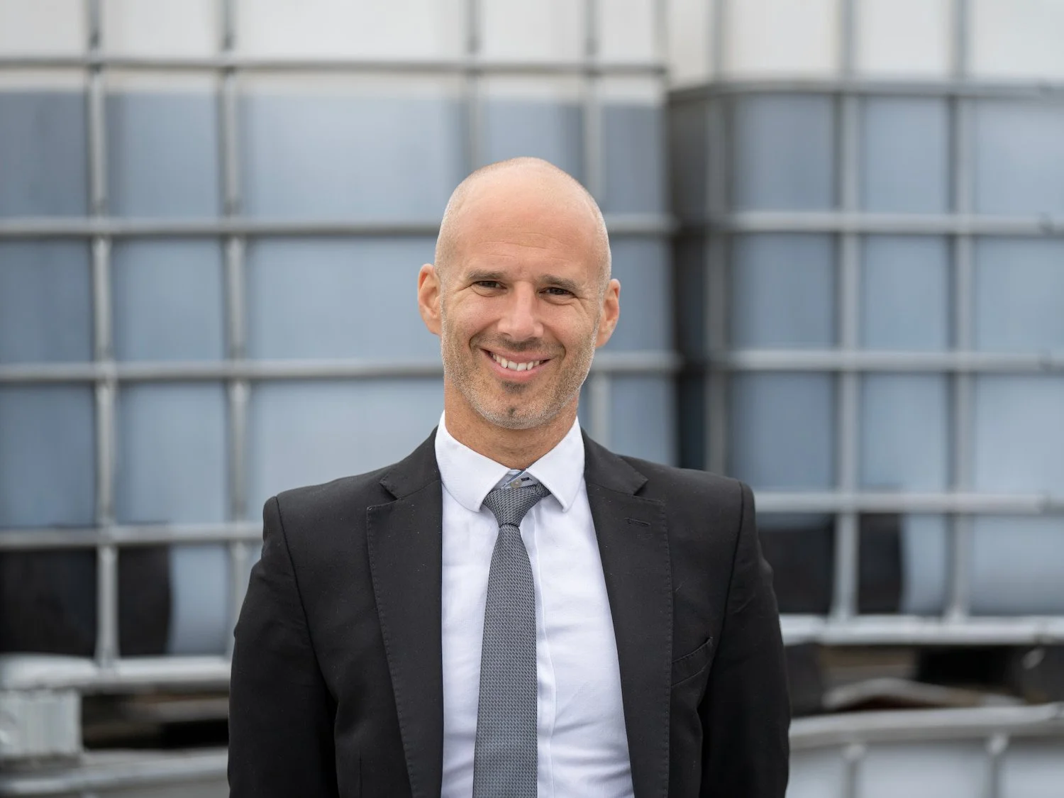 Simon Spiteri, Sales Director at Castle Environmental, smiles in a suit before industrial waste containers in Ilkeston