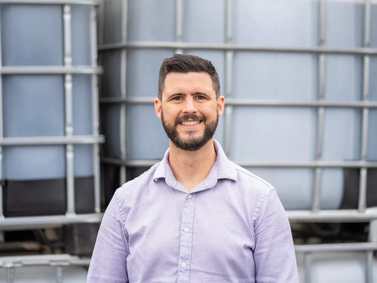 Nathan Ainscough, Technical Sales Manager at Castle Environmental, smiling in a purple shirt before waste containers
