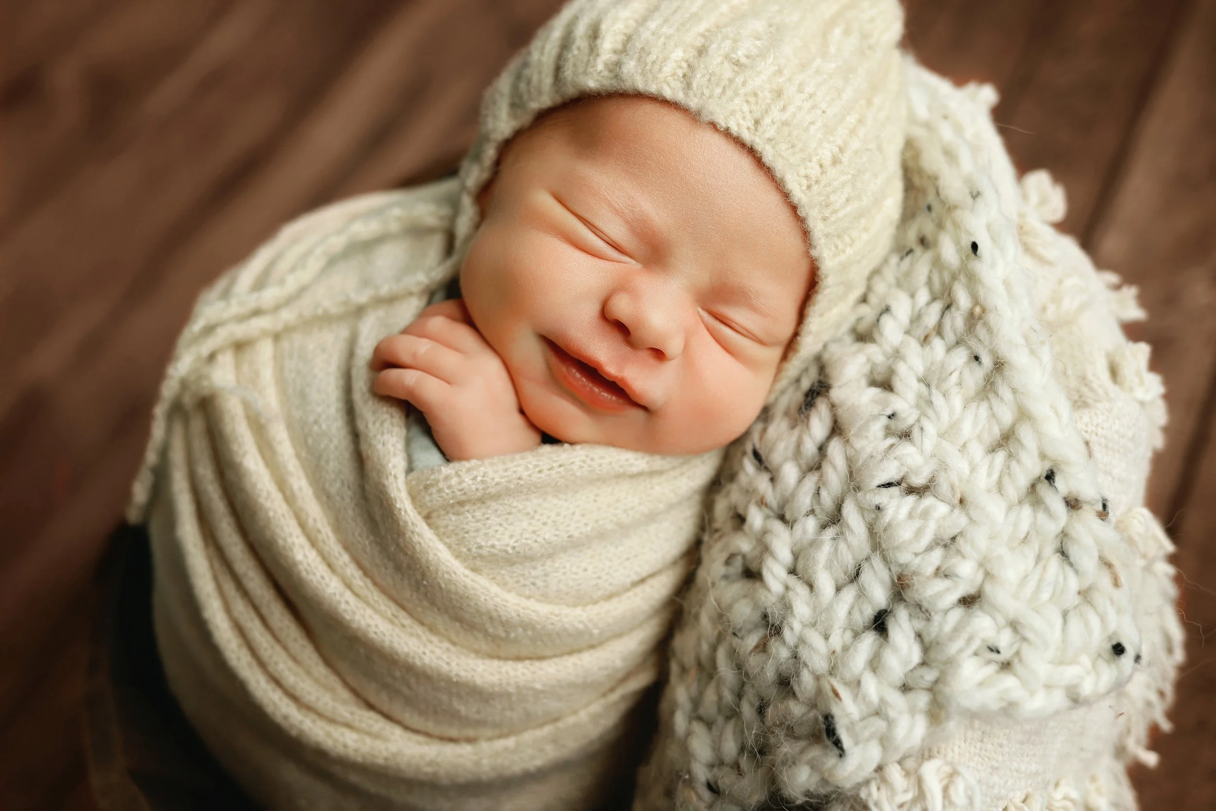 Close-up of a smiling newborn baby boy wrapped in a cream knit blanket and hat, peacefully sleeping during a cozy studio session captured by a Southern Illinois photographer.