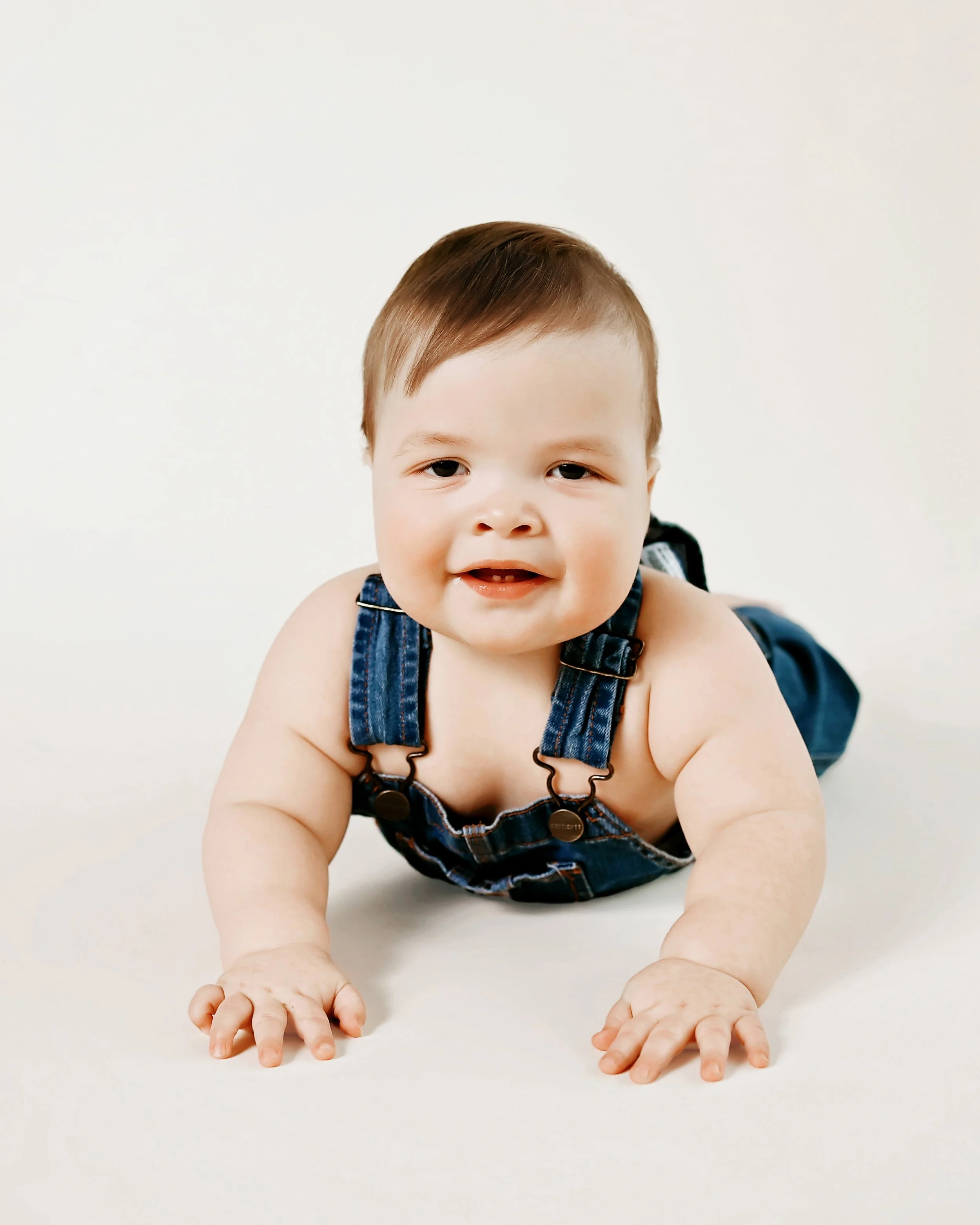 baby boy in carhartt overalls laying on a beige background