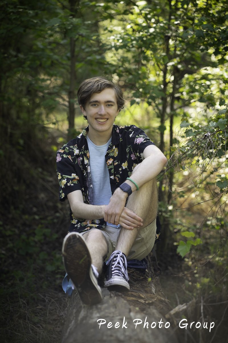 young man on a log grabbing one bent knee