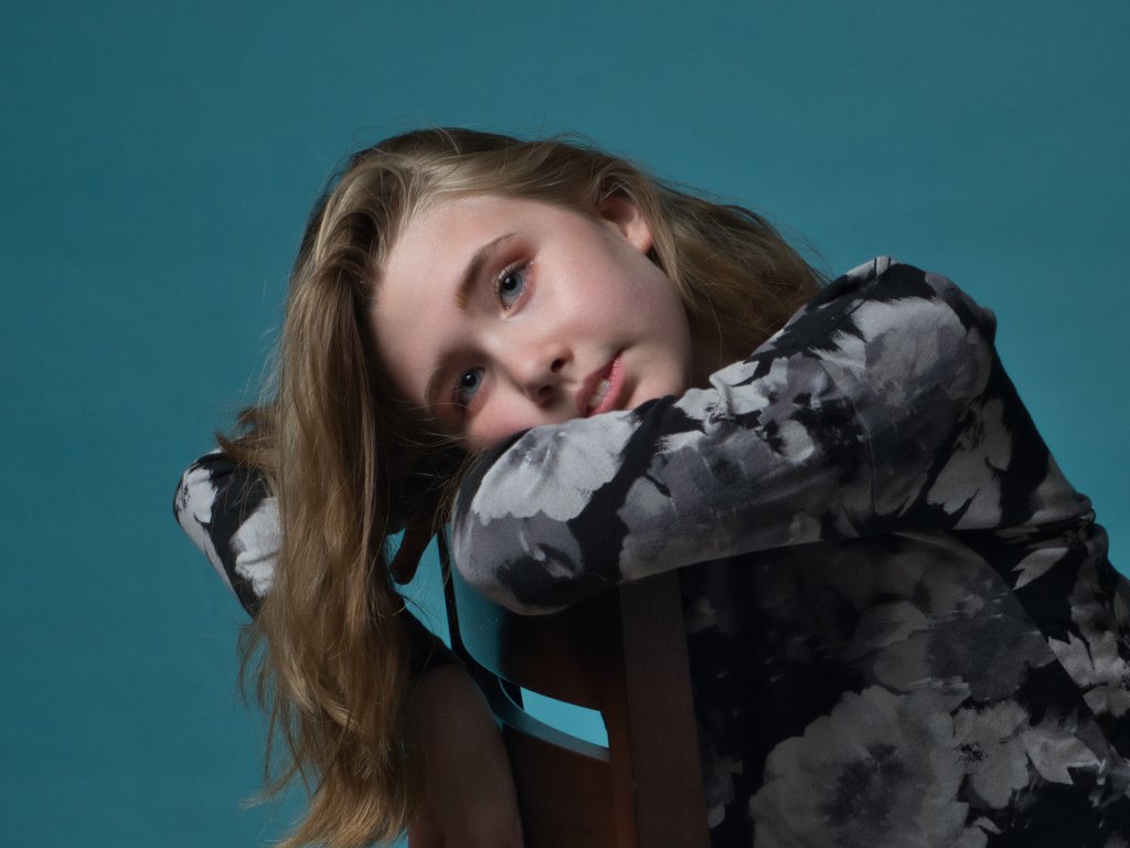 Young blonde girl leaning on a chair with a blue background