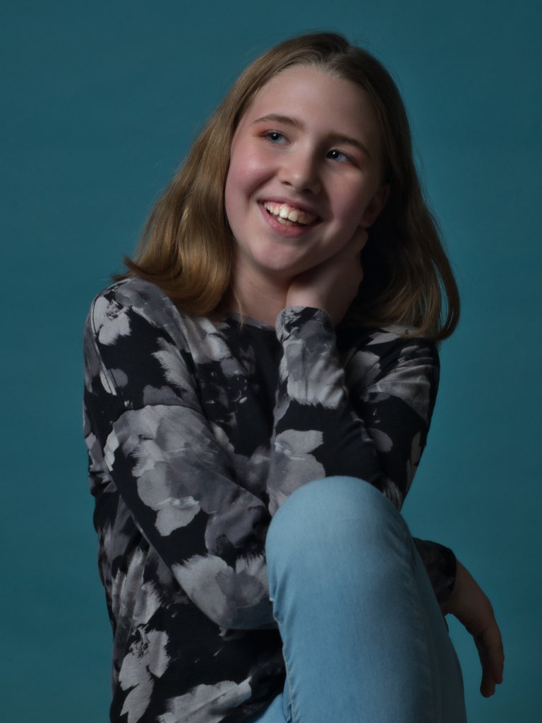 Young girl laughing sitting down with a blue background