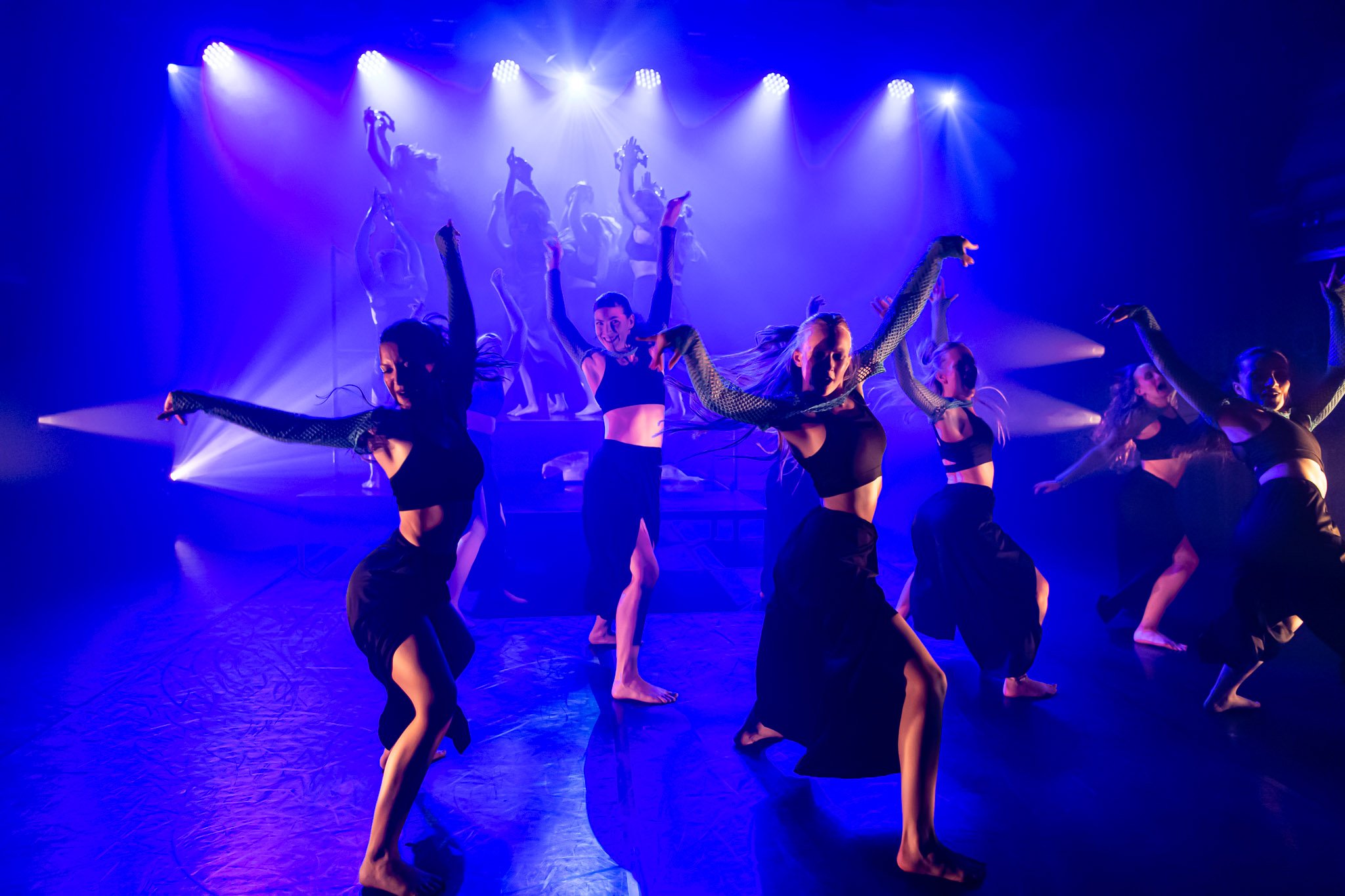 Dancers performing on stage with dramatic lighting and blue hues.