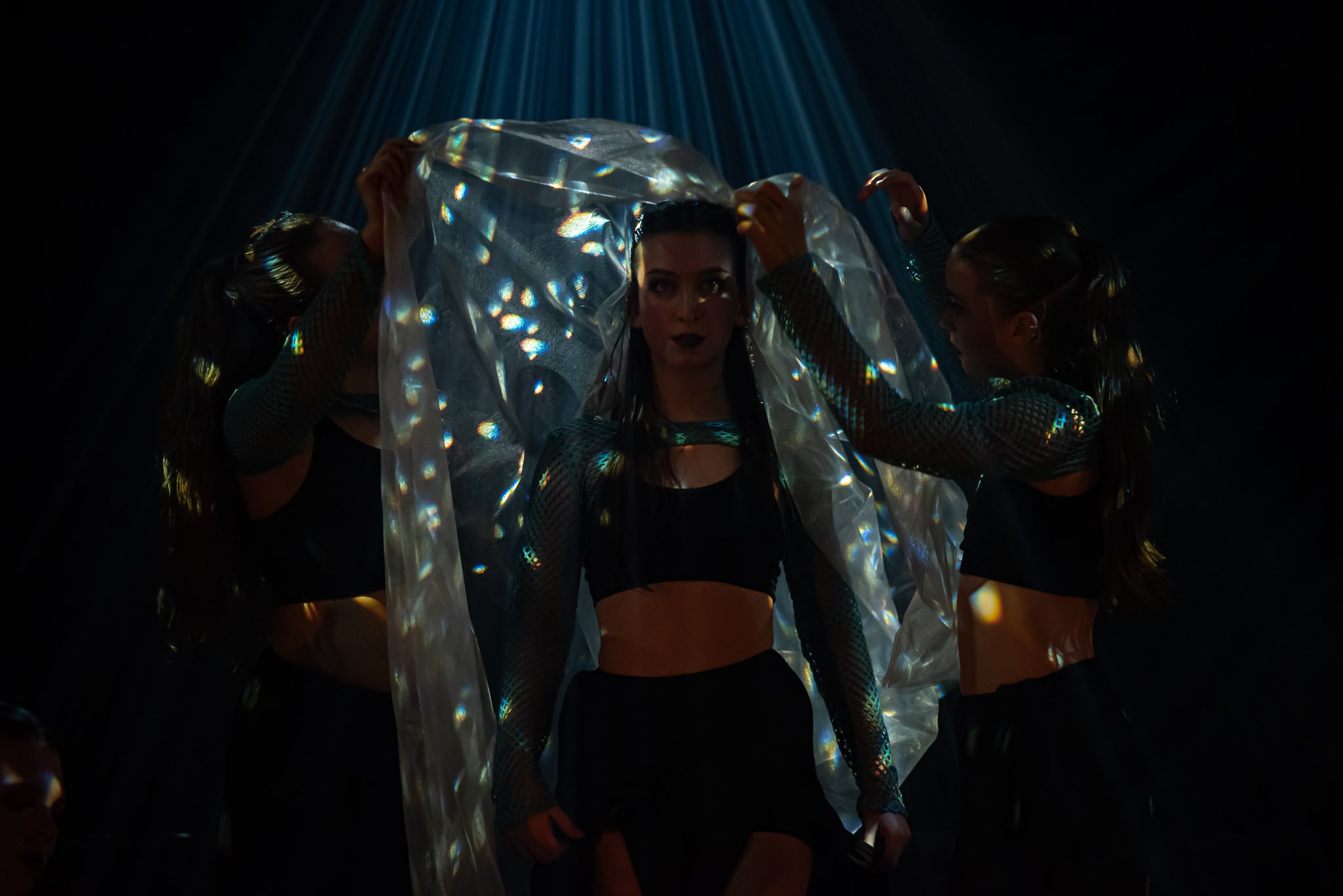 Performers under spotlight with reflective fabric and dark outfits
