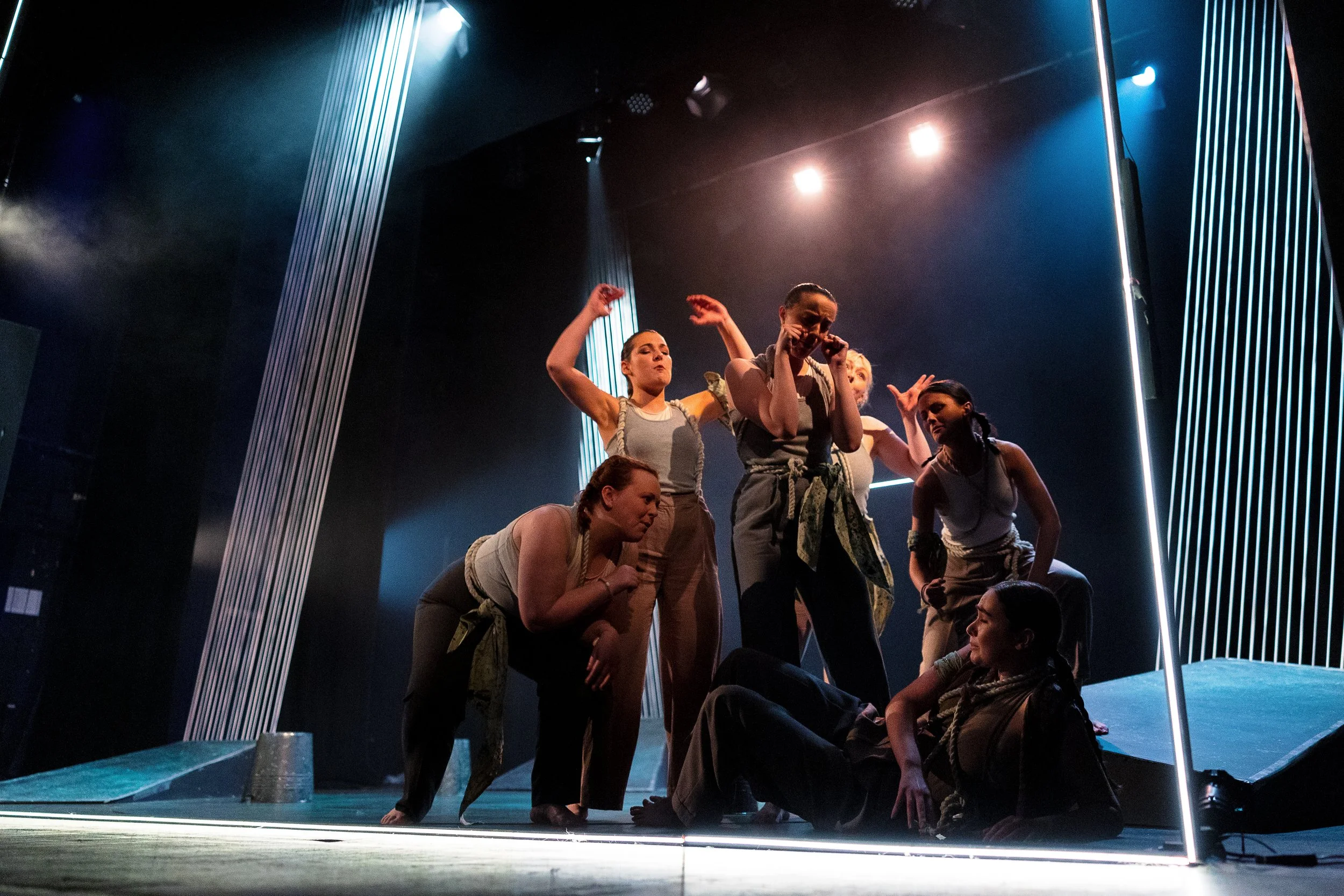 Group of dancers on stage, performing under dramatic lighting, in a dynamic pose with expressive movements.