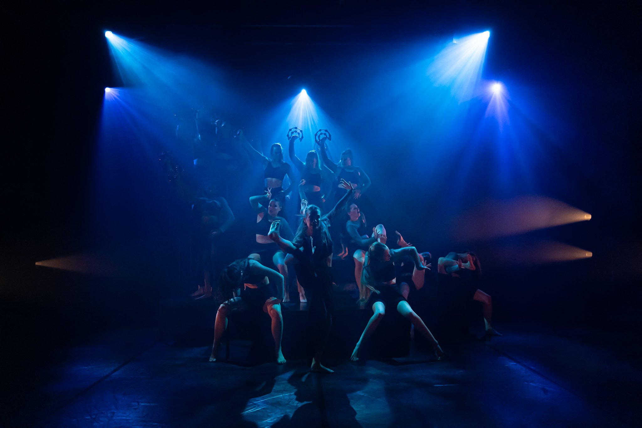 Dancers performing on stage with dramatic blue lighting and shadows.