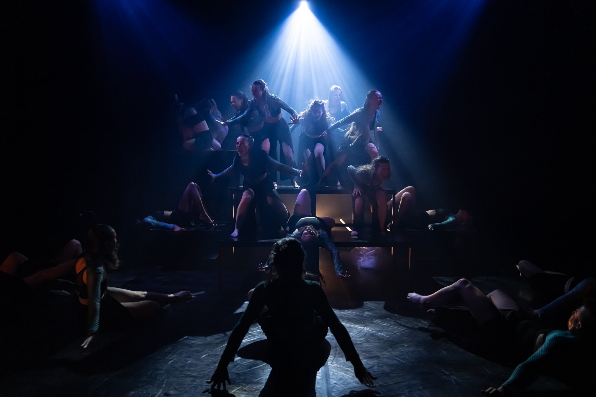 Silhouetted dancers on stage with dramatic blue lighting, various poses.
