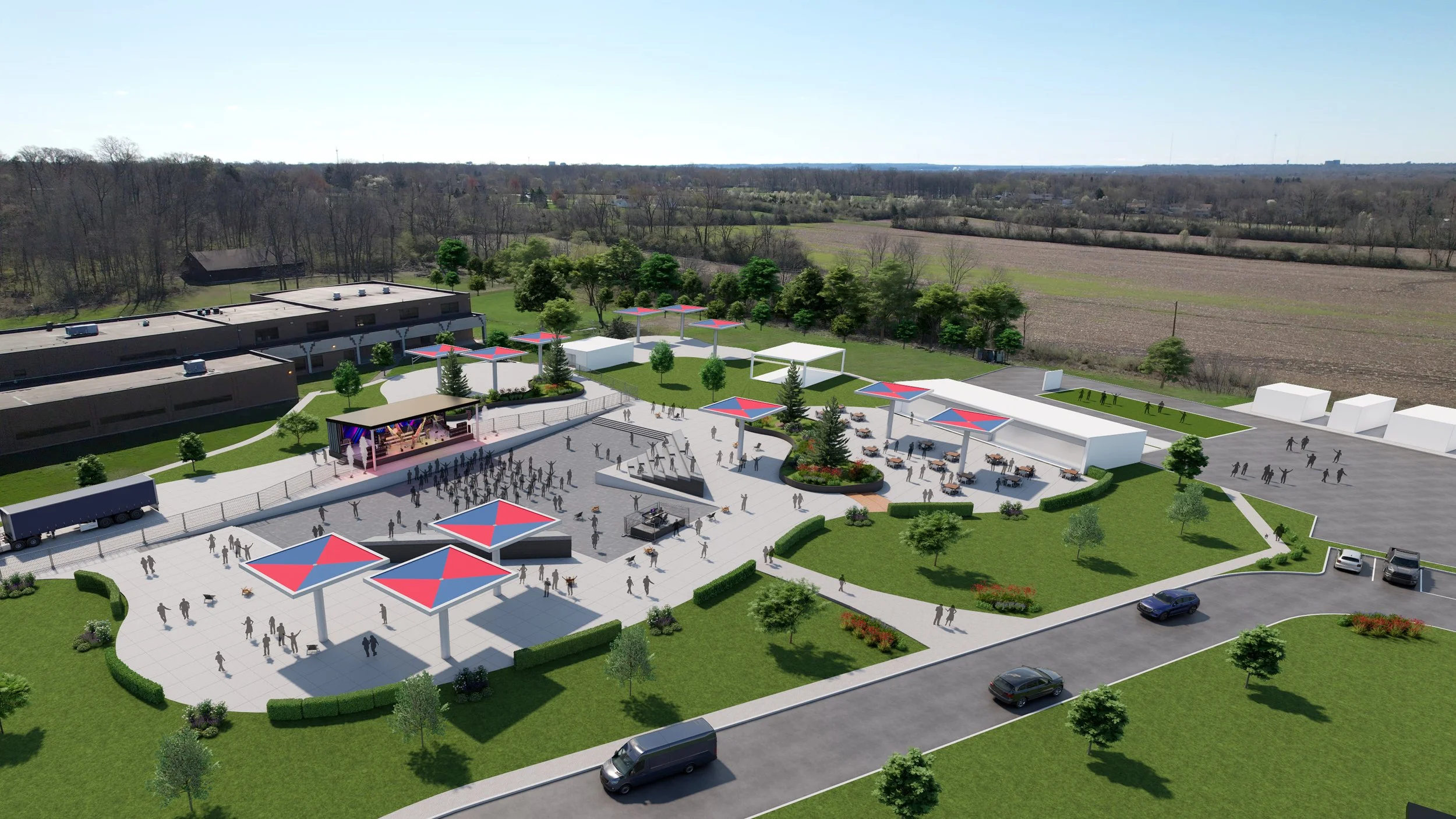 An aerial view of an outdoor event space with a stage, seating, shaded areas, and green landscaping on a sunny day.