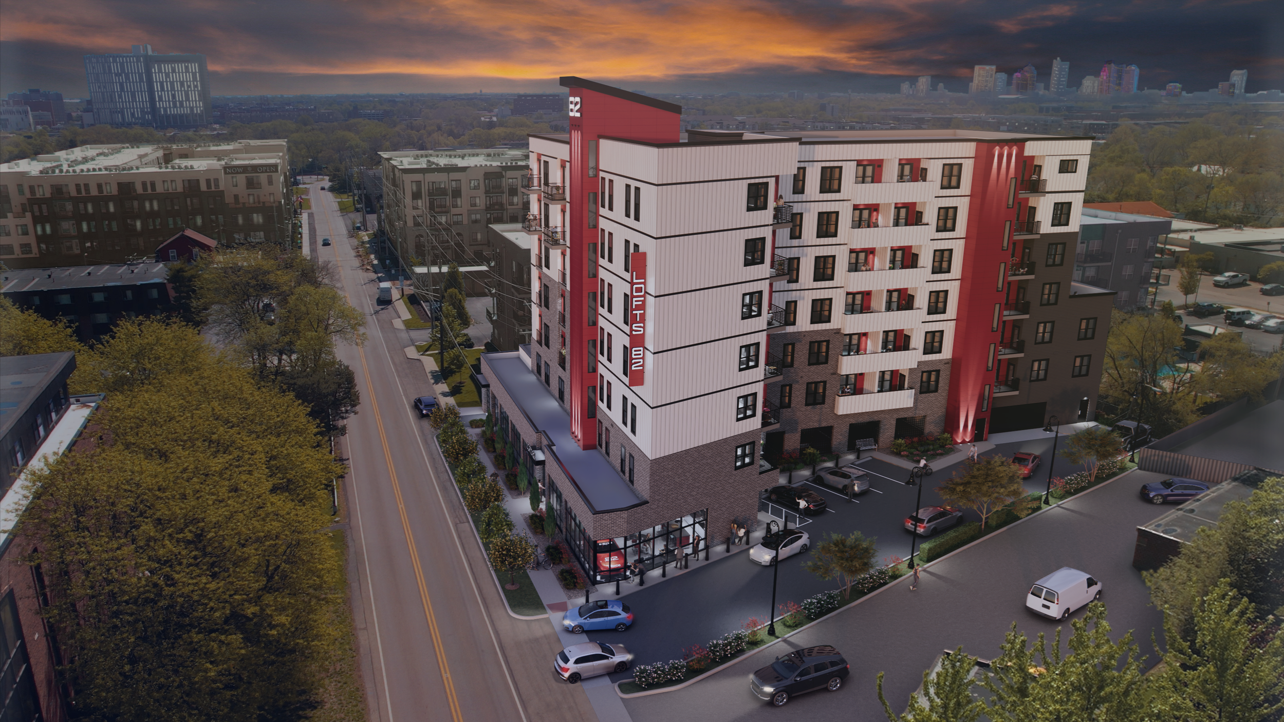 A modern multi-story apartment building with a red and white exterior, located on a city street at sunset. The building has a sign that reads 'Lofts' and features balconies, a parking lot with cars, and surrounding trees.