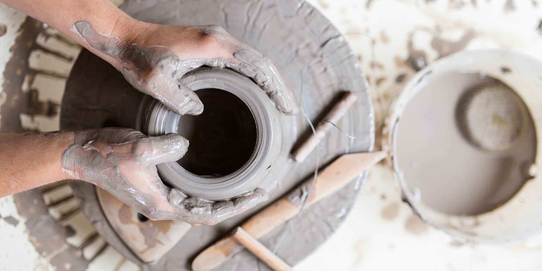 Hands covered in clay shaping a pottery piece on a potter's wheel in a pottery studio.