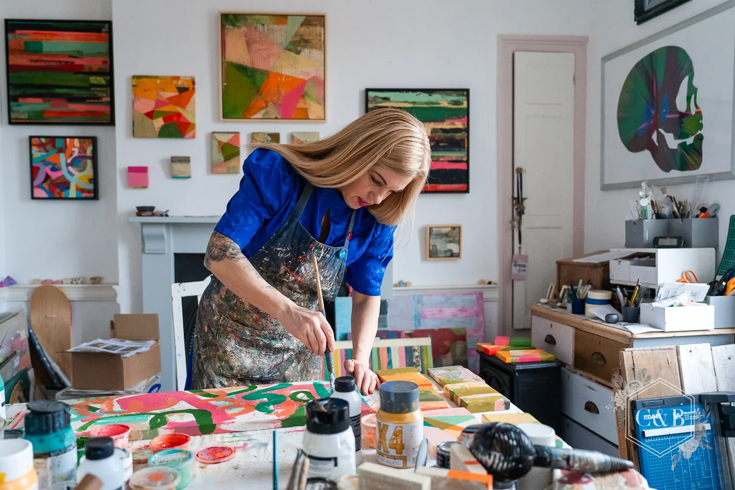 An artist surrounded by colourful paint pots using a paintbrush to paints an abstract piece of art in their studio in Chippenham