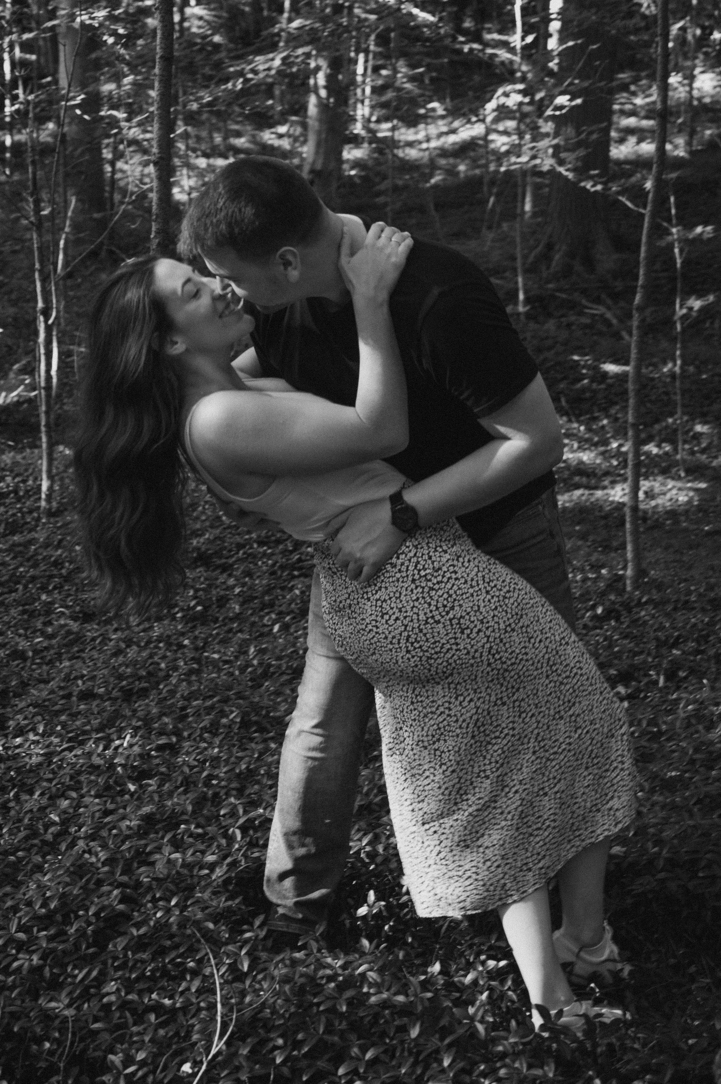 A couple sharing a romantic moment in a forest, with the man dipping the woman as they touch foreheads.