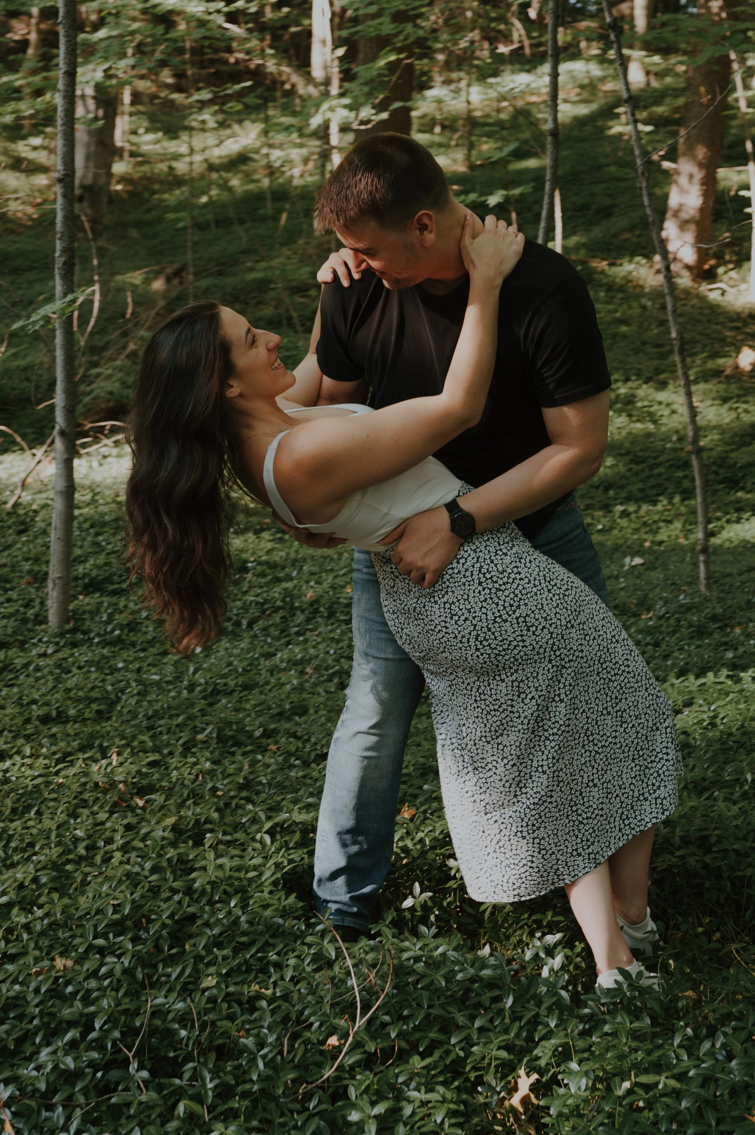 A couple dancing closely in a wooded outdoor setting, smiling and looking at each other.