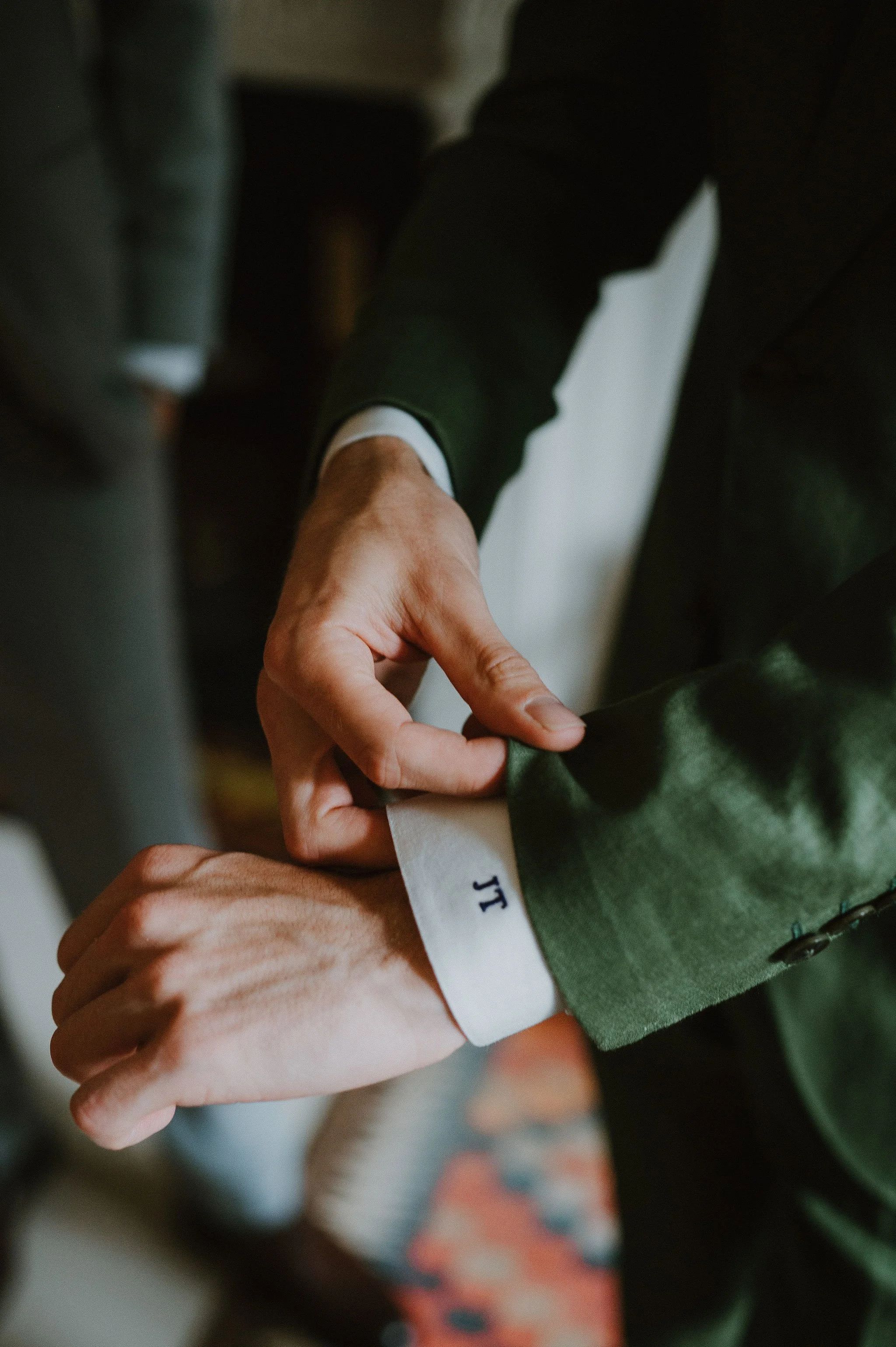 Close-up of a person adjusting their white wristband with navy blue initials 'J T' on a green jacket.